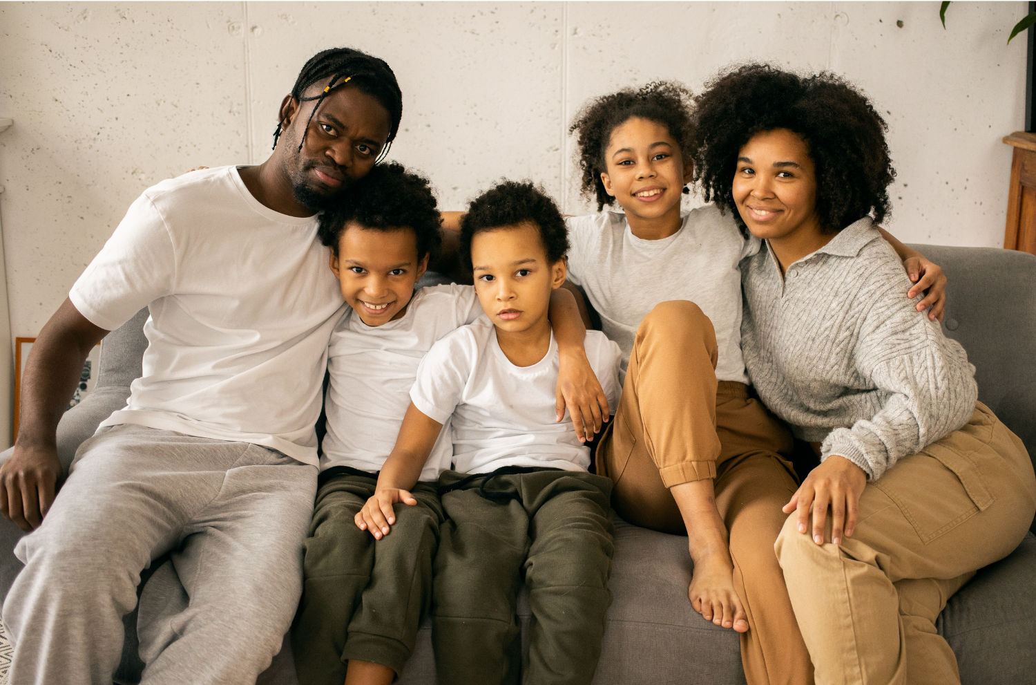 A family of two parents and 3 children sit on a couch