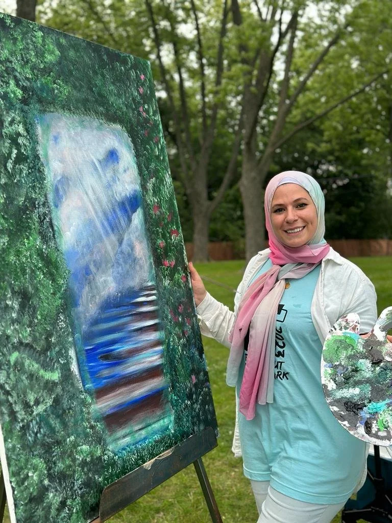 A picture of me standing next to my painting at the festival.