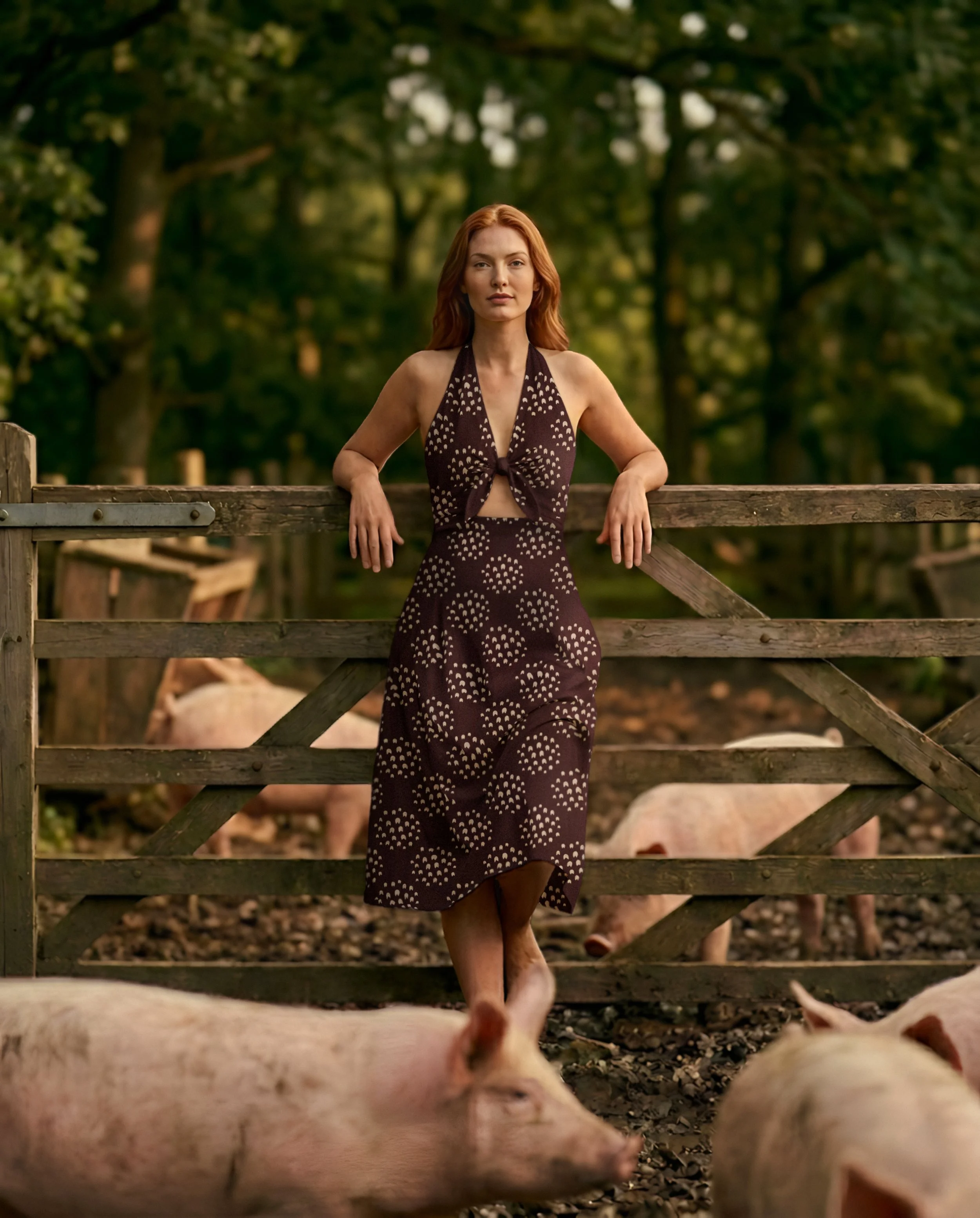 Editorial image of a woman in a muddy pig pen wearing a brown decorative sun dress