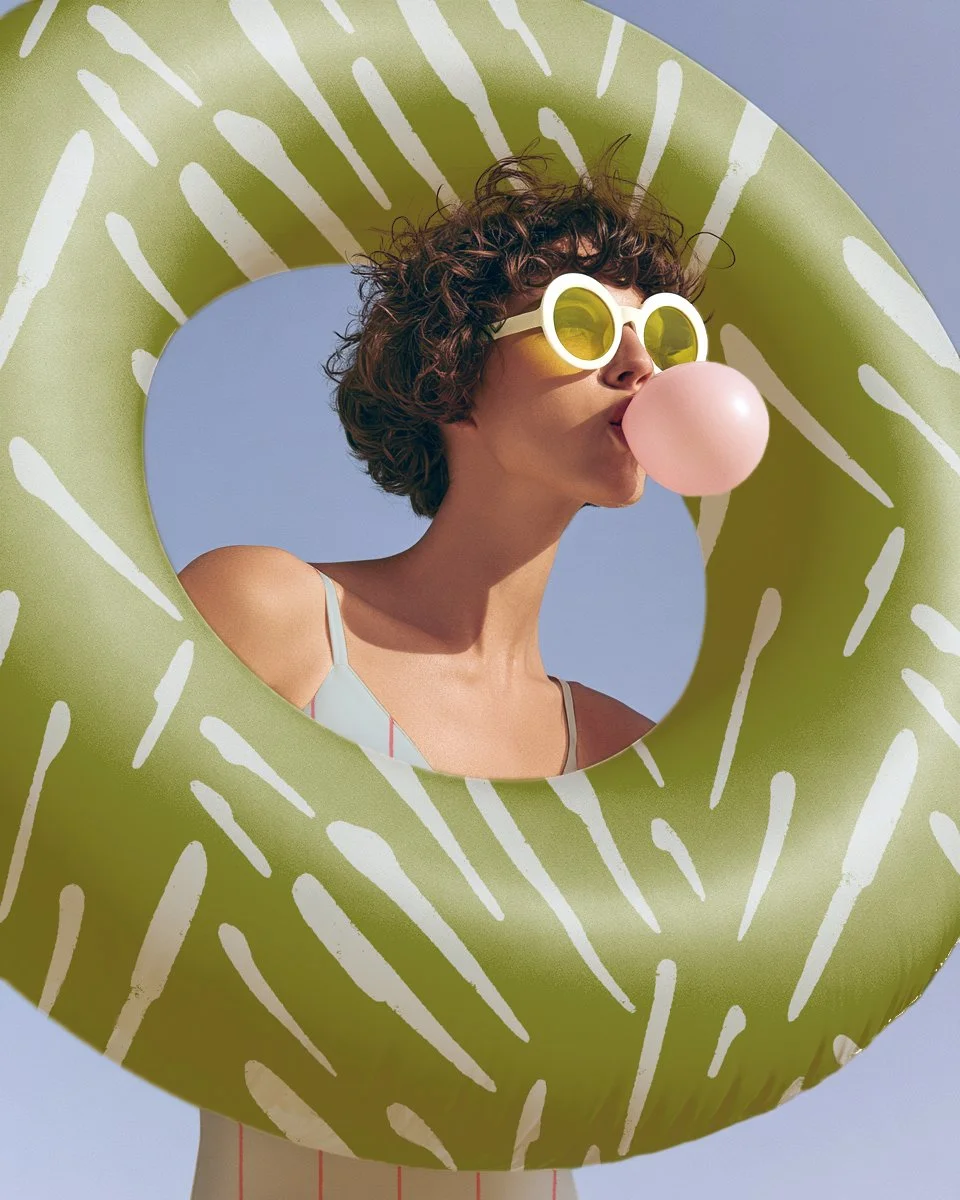 A woman wearing retro sunglasses blowing bubblegum through a green patterned inflatable pool ring