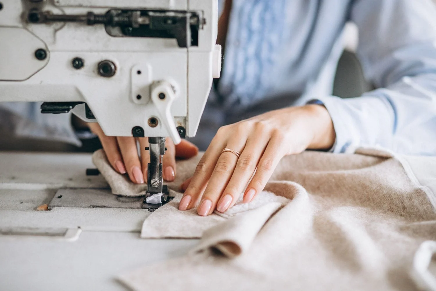 Person sewing beige fabric on a sewing machine.
