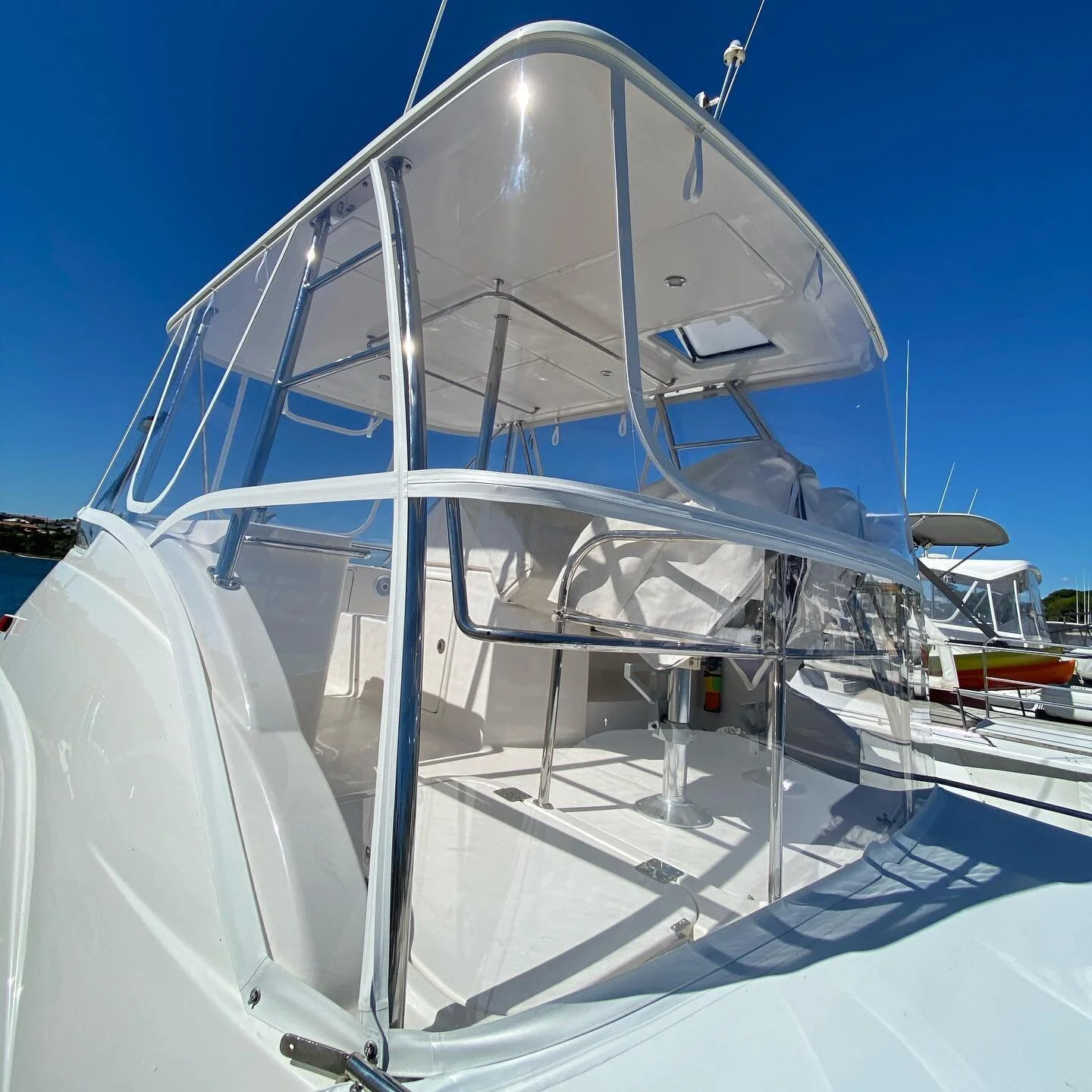 A white boat docked at a marina under a clear blue sky, with shiny metal railings and a canopy covering the upper deck.
