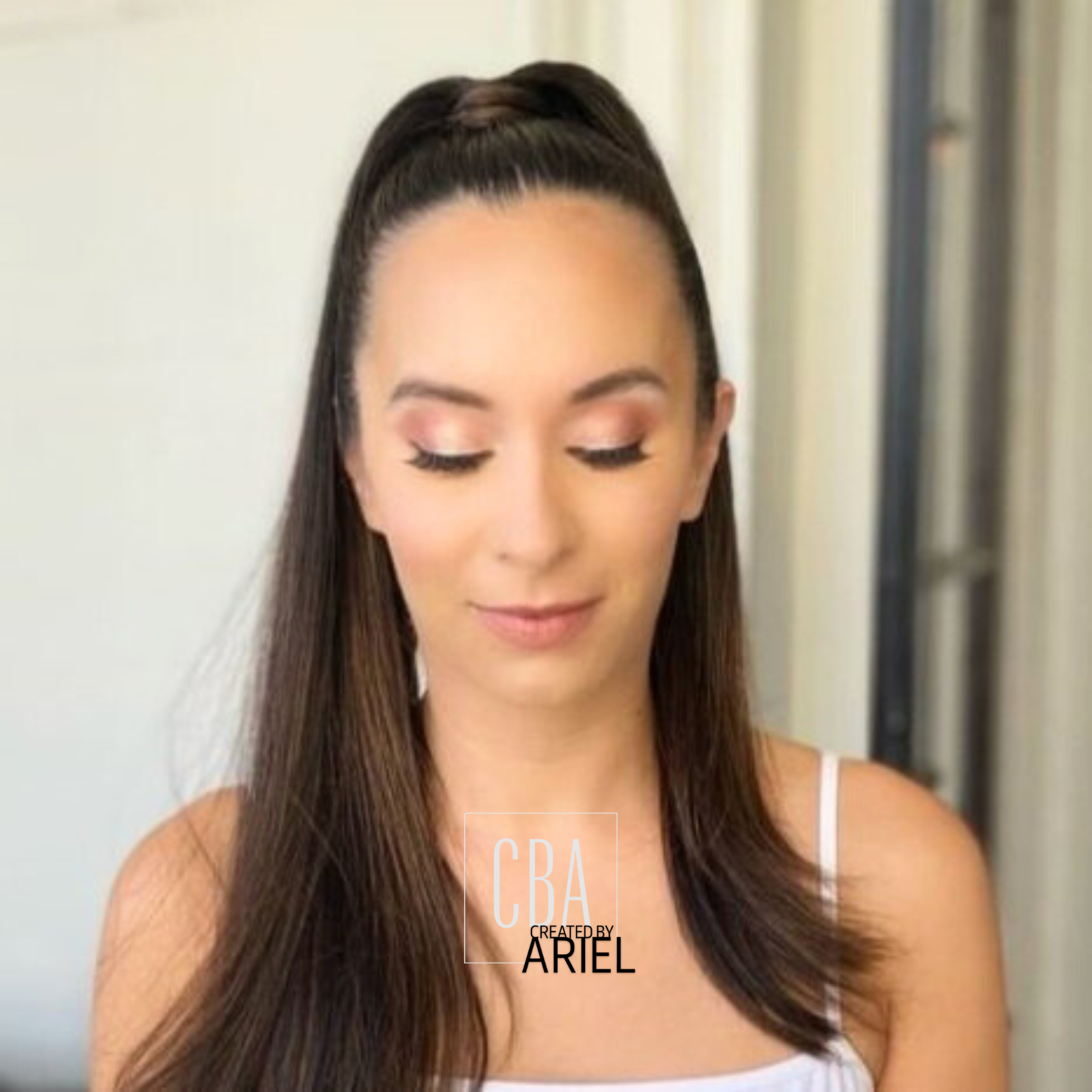 Close-up of a woman with long brown hair, eyes closed, wearing makeup, in an indoor setting.