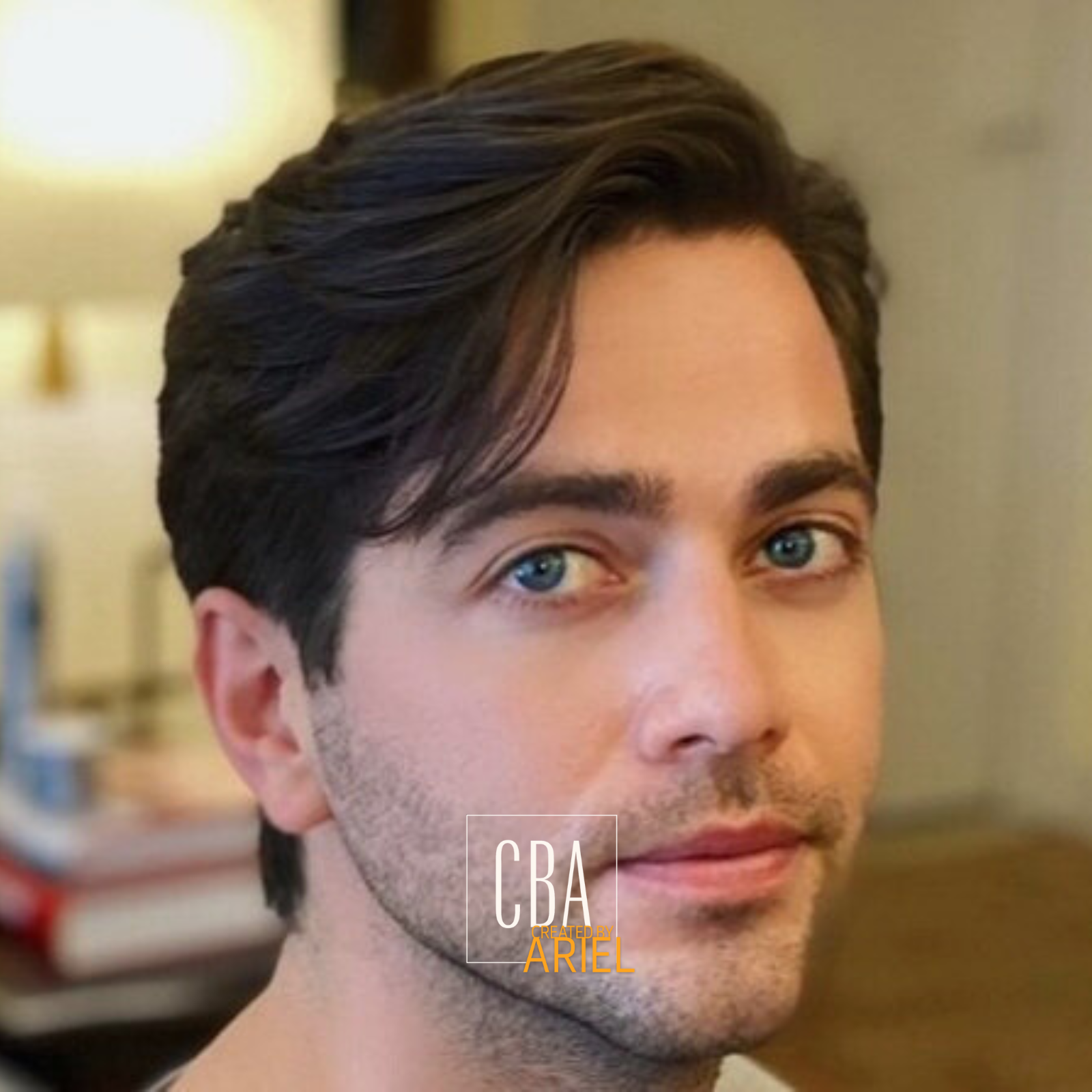 Close-up of a young man with blue eyes, dark brown hair, light facial hair, and a slight smile.