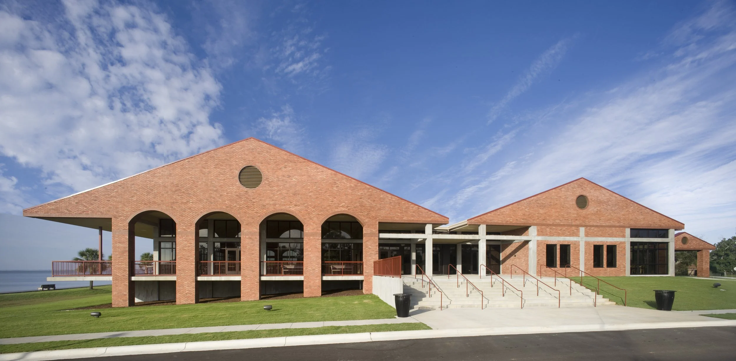 Red brick building with arched windows, stairs, and a green lawn under a partly cloudy blue sky.