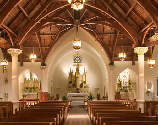 Inside a church with wooden arched ceiling, white columns, and religious altars at the front.