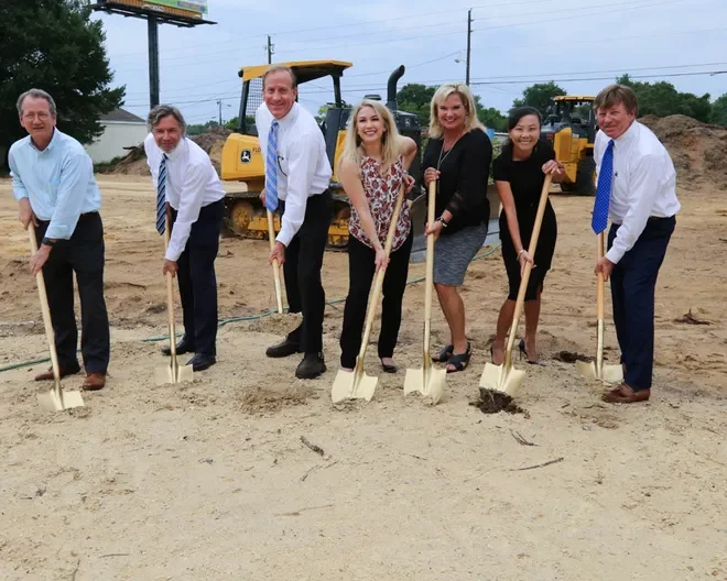 People participating in a groundbreaking ceremony holding golden shovels, with construction equipment in the background.