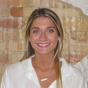 A woman with long blonde hair smiling in front of a brick wall.