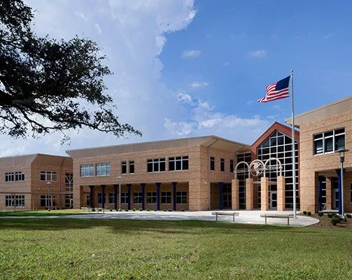 Exterior view of a school building with an American flag, trees, and a partly cloudy sky.
