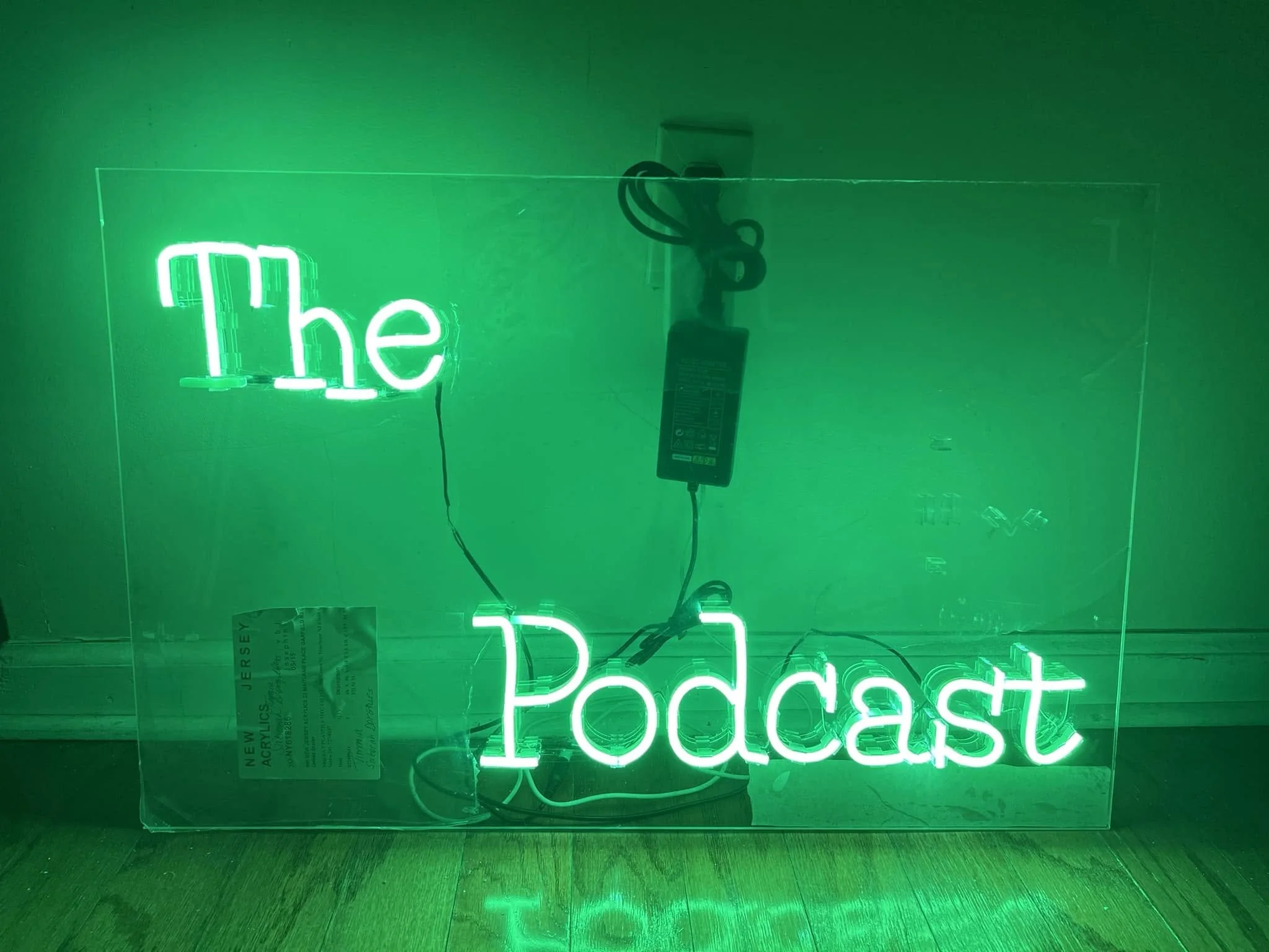 Green neon sign with the words 'the Podcast' illuminated, reflecting on a dark surface.