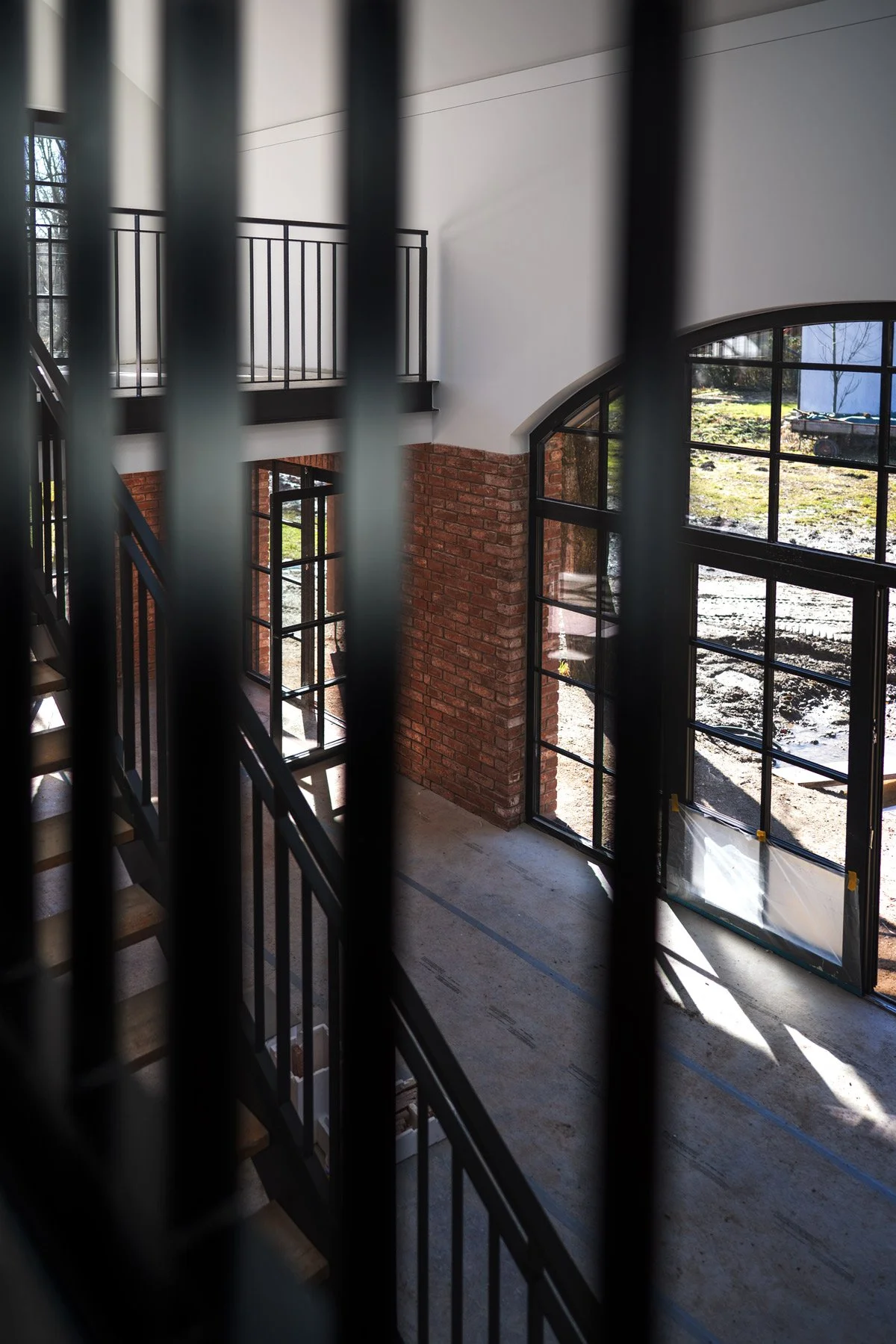 Innenansicht eines Gebäudes mit großen Fensterflächen, einem offenen Treppenaufgang und einer Mischung aus Ziegel- und weißer Wand, vermutlich im Bau oder Renovierungsphase.