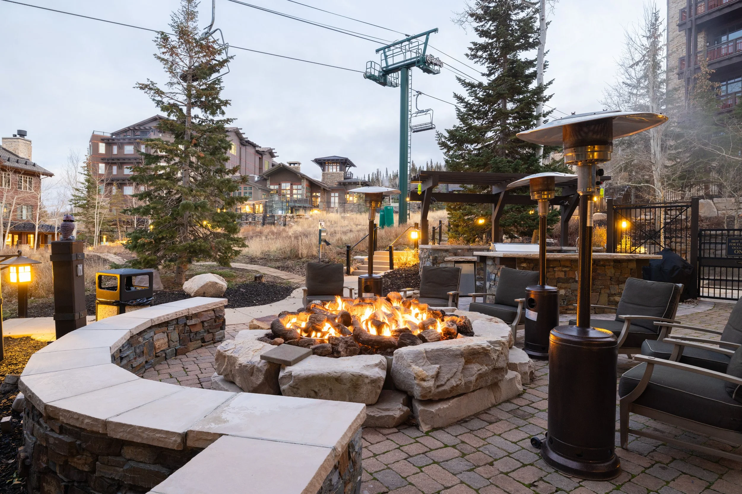 Slope-side fire pit with seating and heat lamps — a gathering place at twilight