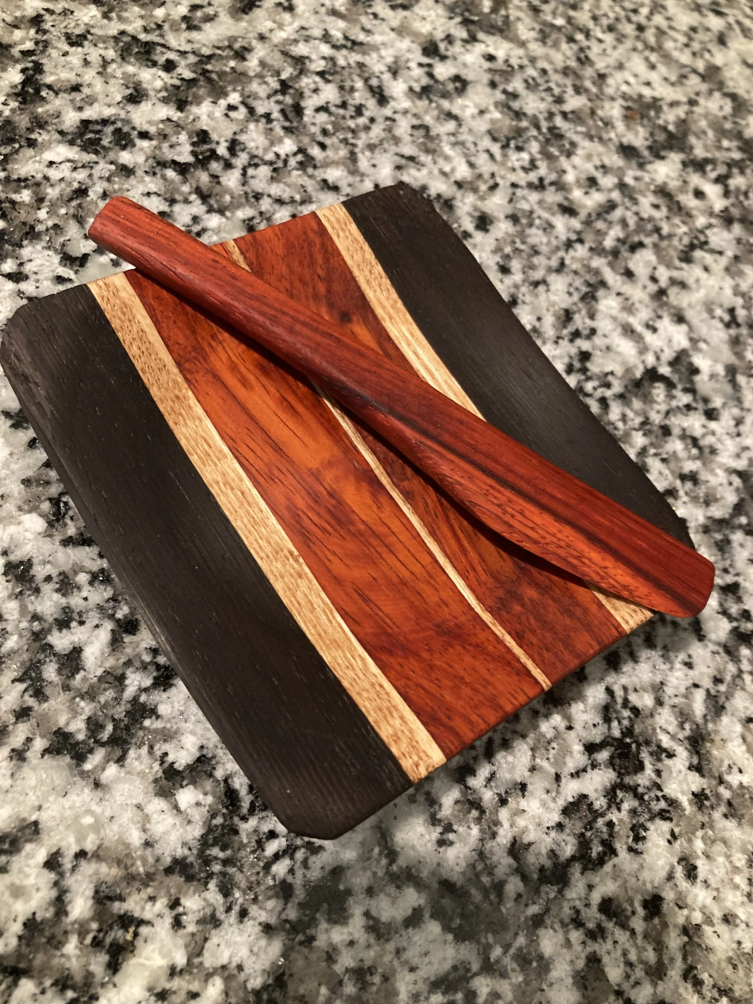 A wooden hair stick resting on a striped wooden block on a granite countertop.