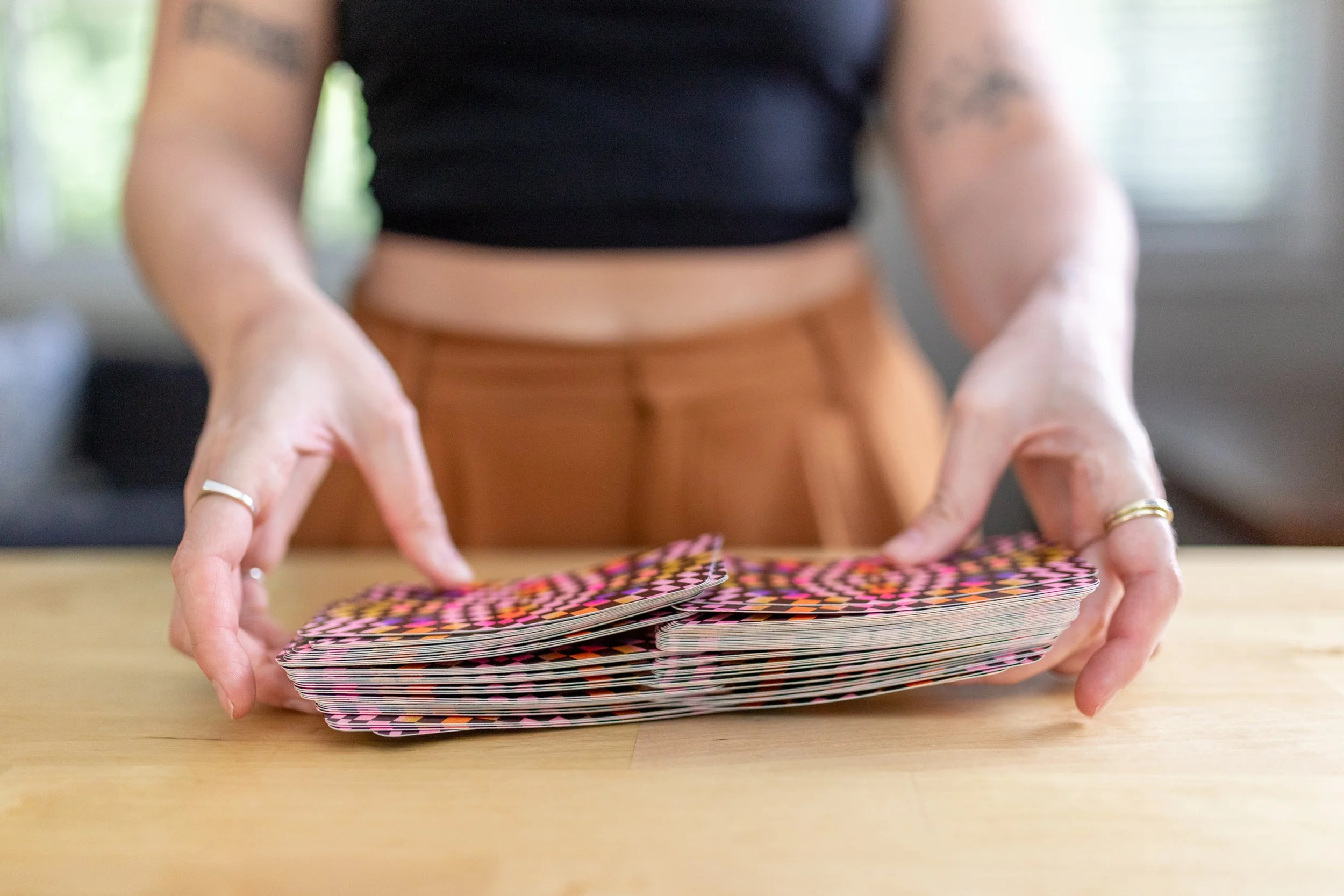 Person handling a stack of colorful cards on a wooden table.