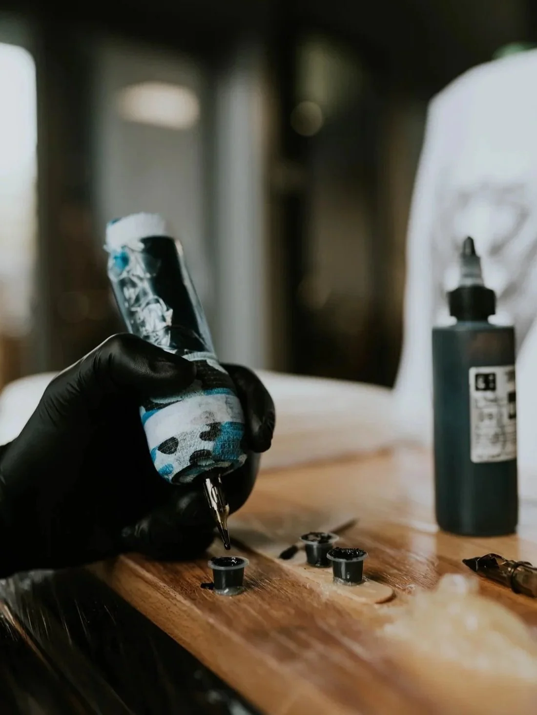 Tattoo artist in black gloves creating a tattoo on a person's arm.