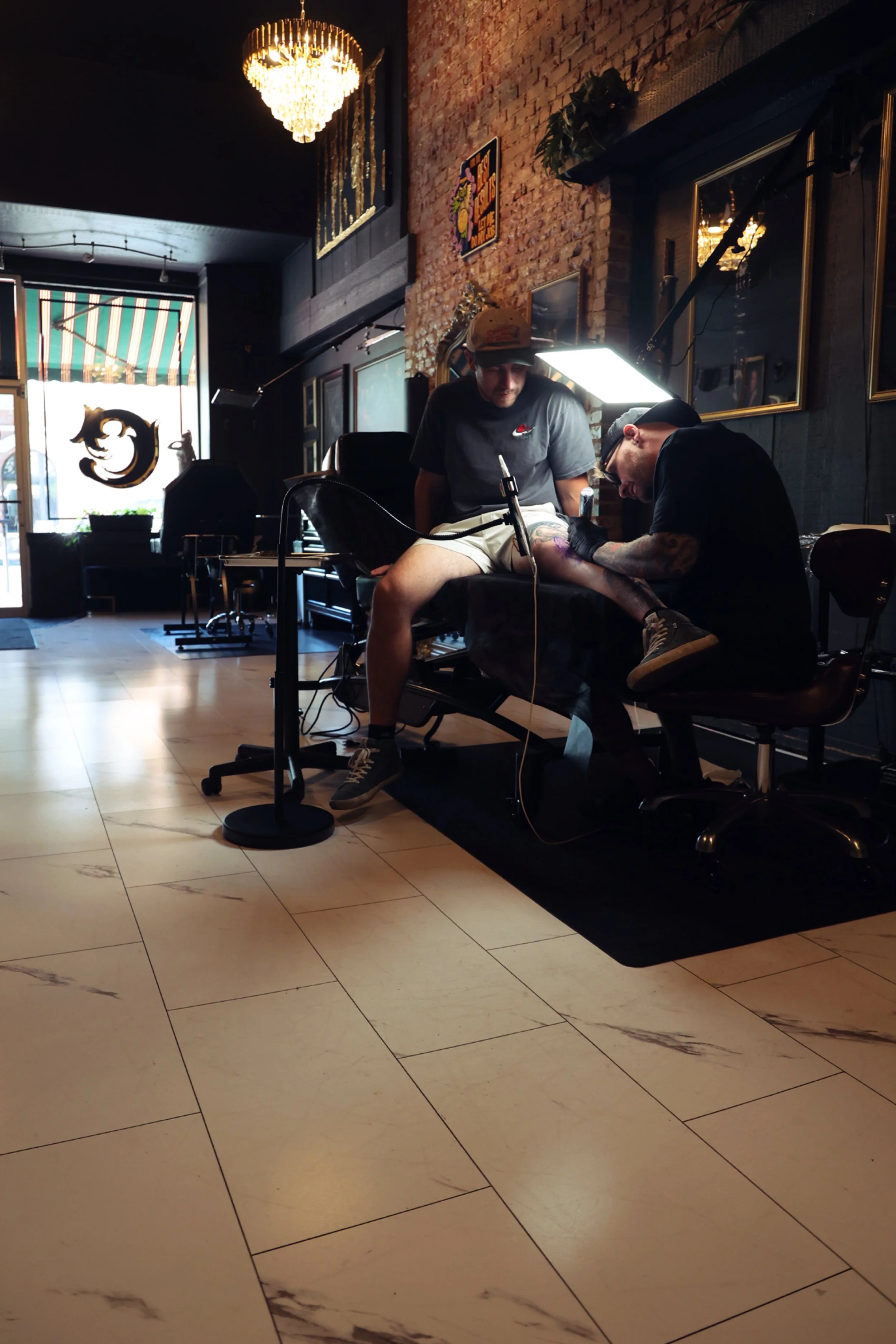 An expert tattoo artist is tattooing a black and gray realism tattoo on a clients leg as the client enjoys the experience of a comfortable client bed, listening to music and admiring the sophisticated ambiance in Chariot's downtown Boise studio. 