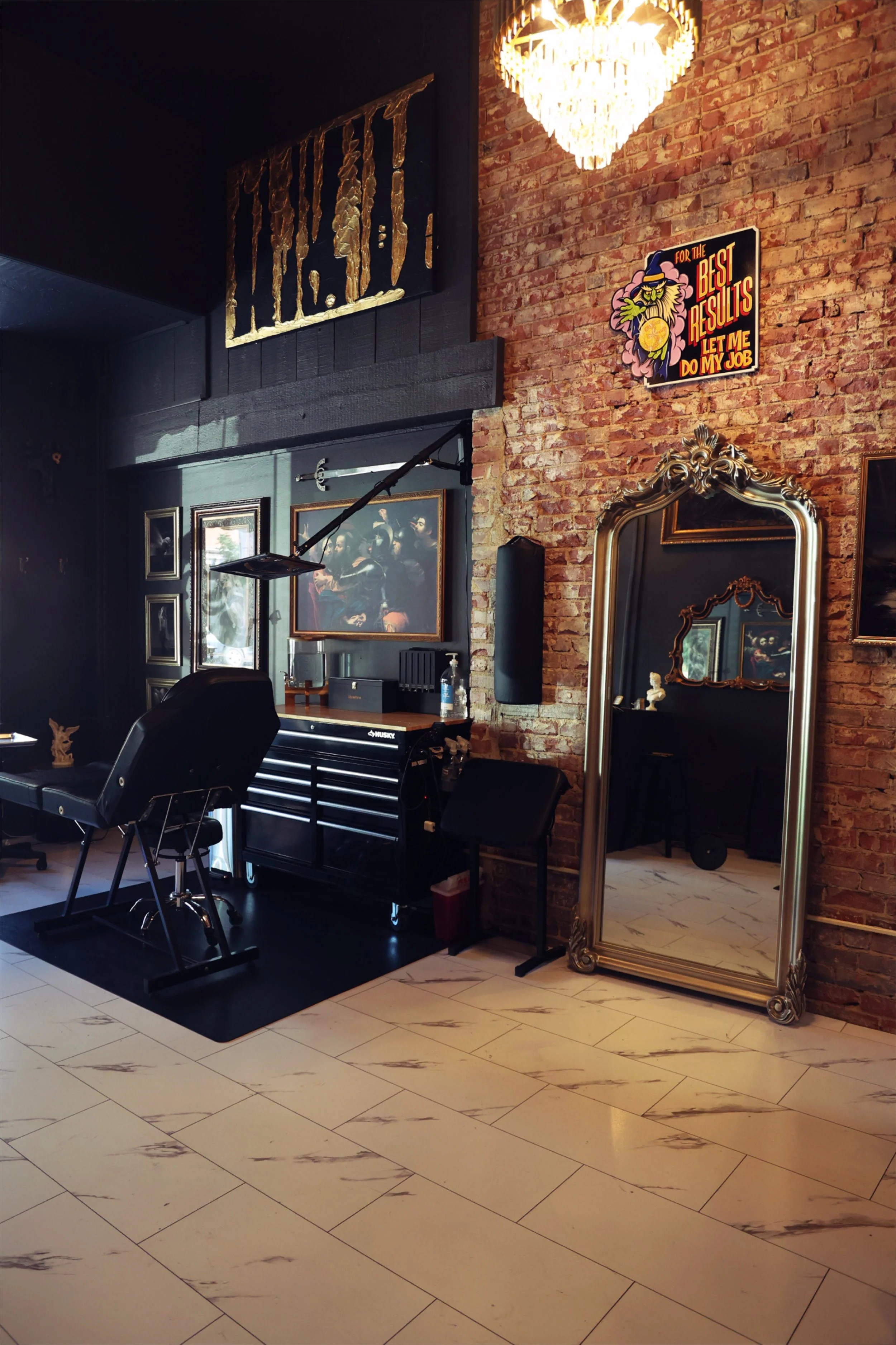 White marble floors stretch beneath large organized tattoo stations in a moody glow from the gold chandeliers above in Chariot's Boise downtown studio. 