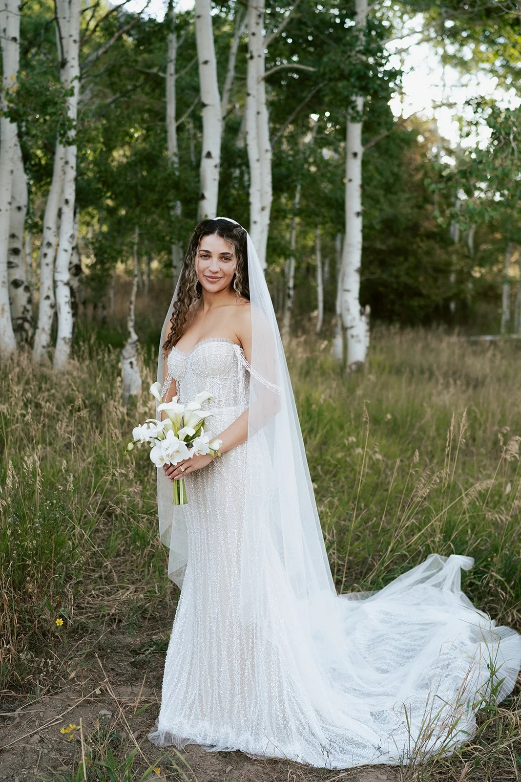 a bride in a beaded wedding gown holds a modern white bouquet while standing in a grove of aspen trees - poise and ivy imagery