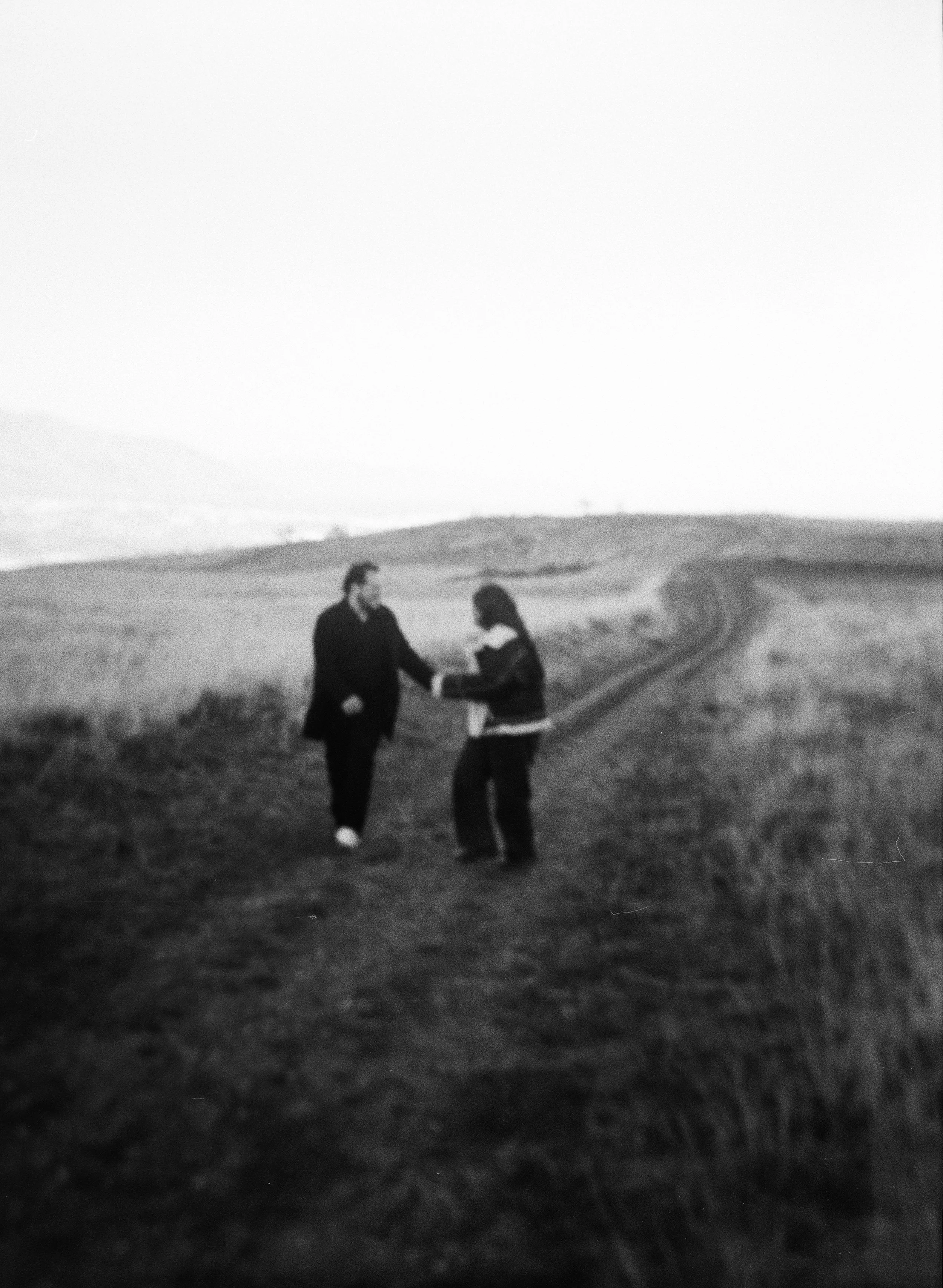 A couple stands together in a softly lit grassy field on black and white medium format film - photography by Poise and Ivy Imagery