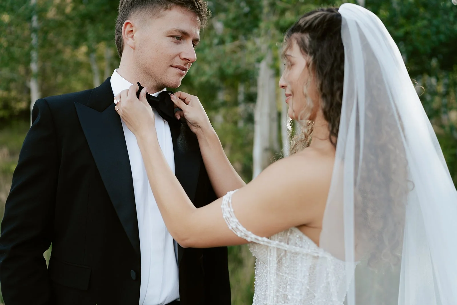 a bride and a groom stand together in a lush aspen grove. the bride wears a beaded wedding gown and the groom wears a tuxedo. Photography by Poise and Ivy Imagery