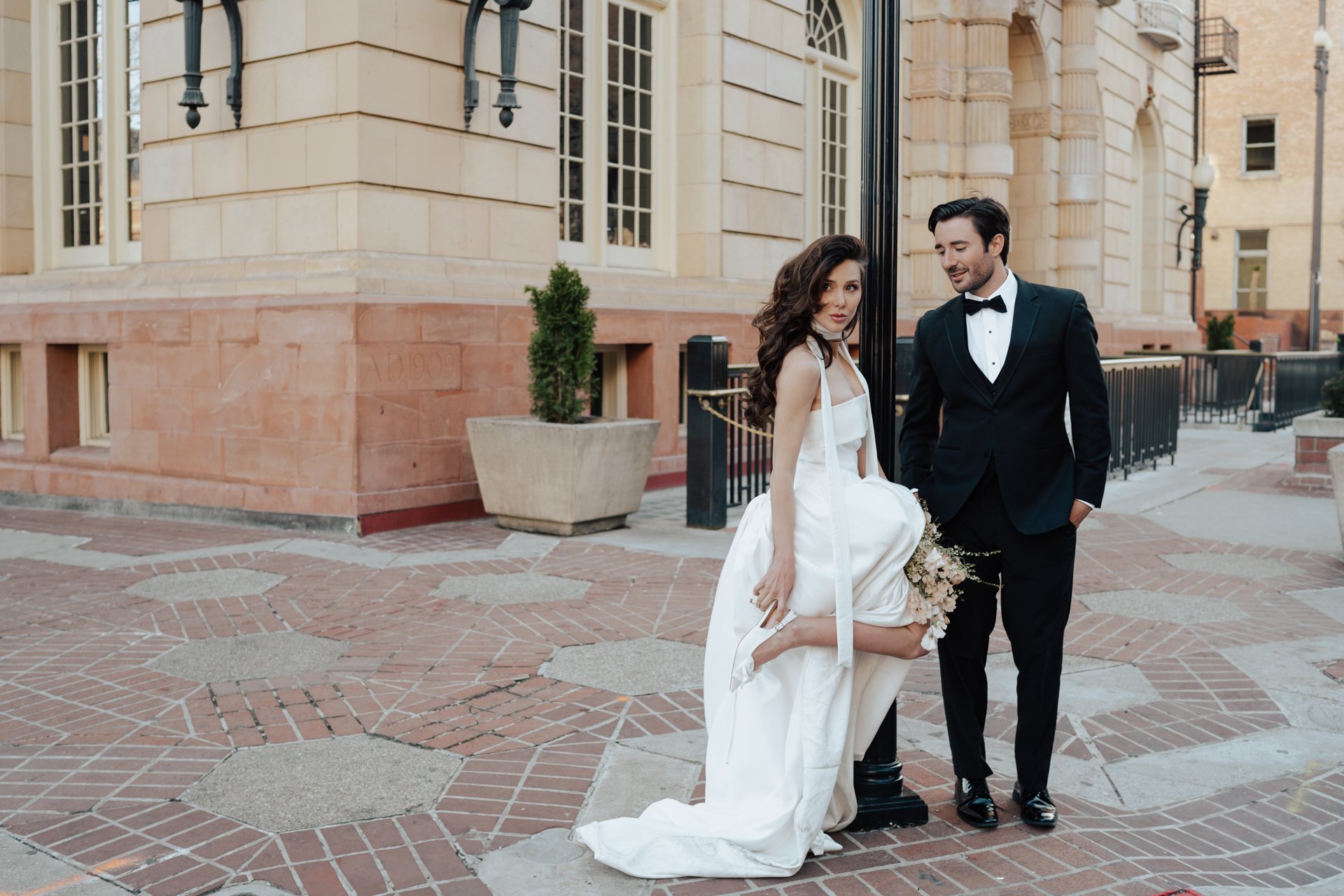 Bride and Groom in classic elegant wedding attire surrounded by beautiful stonework architecture during a downtown formals photoshoot - Poise and Ivy Imagery