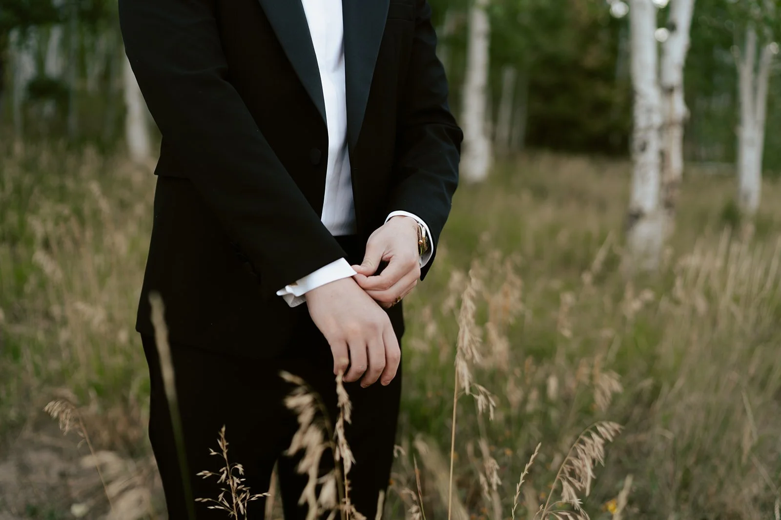 A groom in a black tuxedo from Saint Laurent prepares himself to see his bride for the first time amid a sunlit grove of aspen trees - Poise and Ivy Imagery