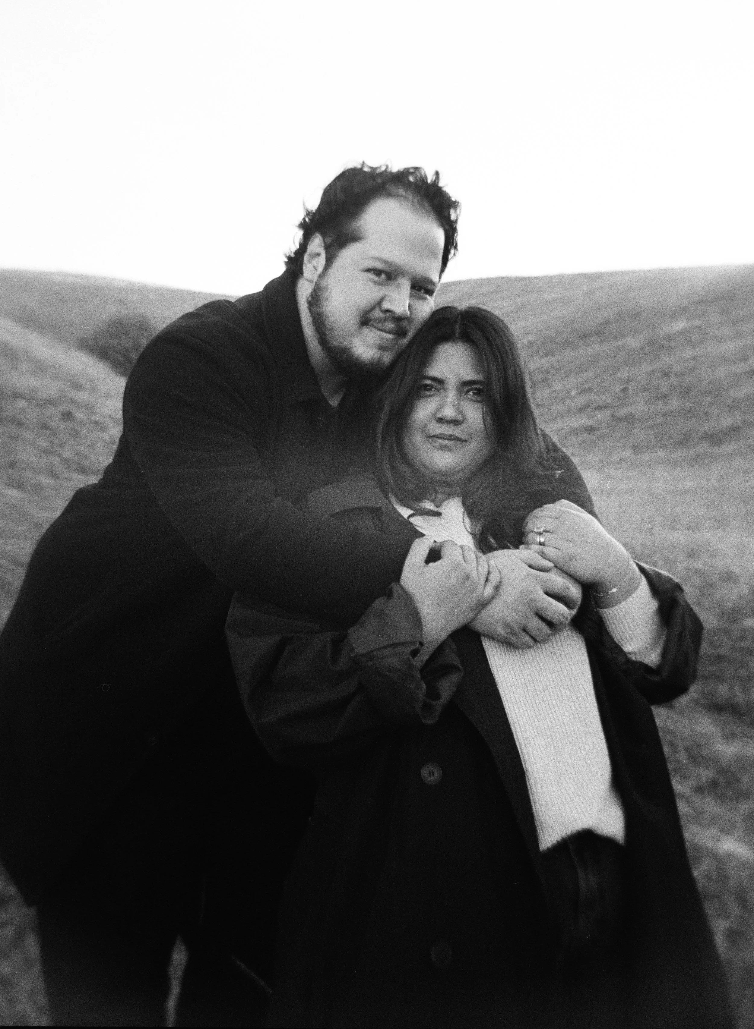 A couple stands together in a softly lit grassy field on black and white medium format film - photography by Poise and Ivy Imagery