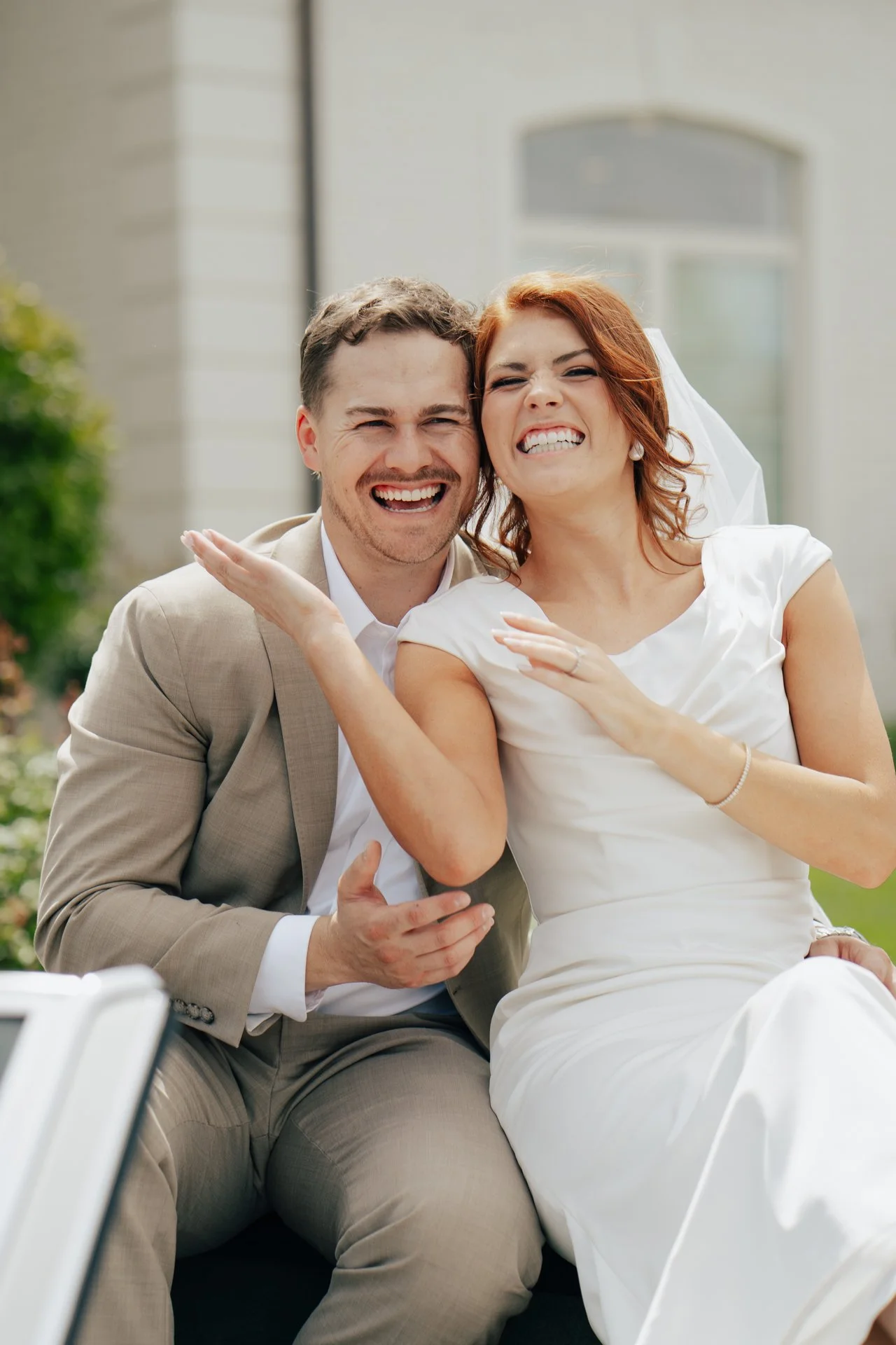 Bride and Groom smiling at photographer Poise & Ivy Imagery on their wedding day in front of their Utah wedding venue, Magnolia