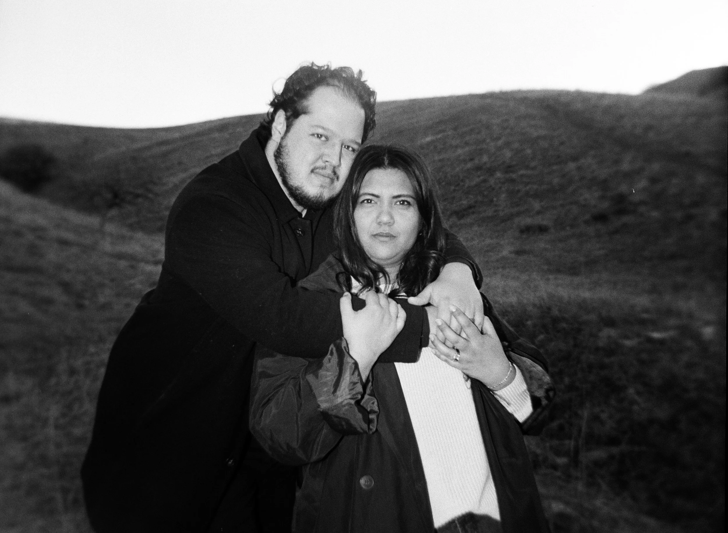 A couple stands together in a softly lit grassy field on black and white medium format film - photography by Poise and Ivy Imagery
