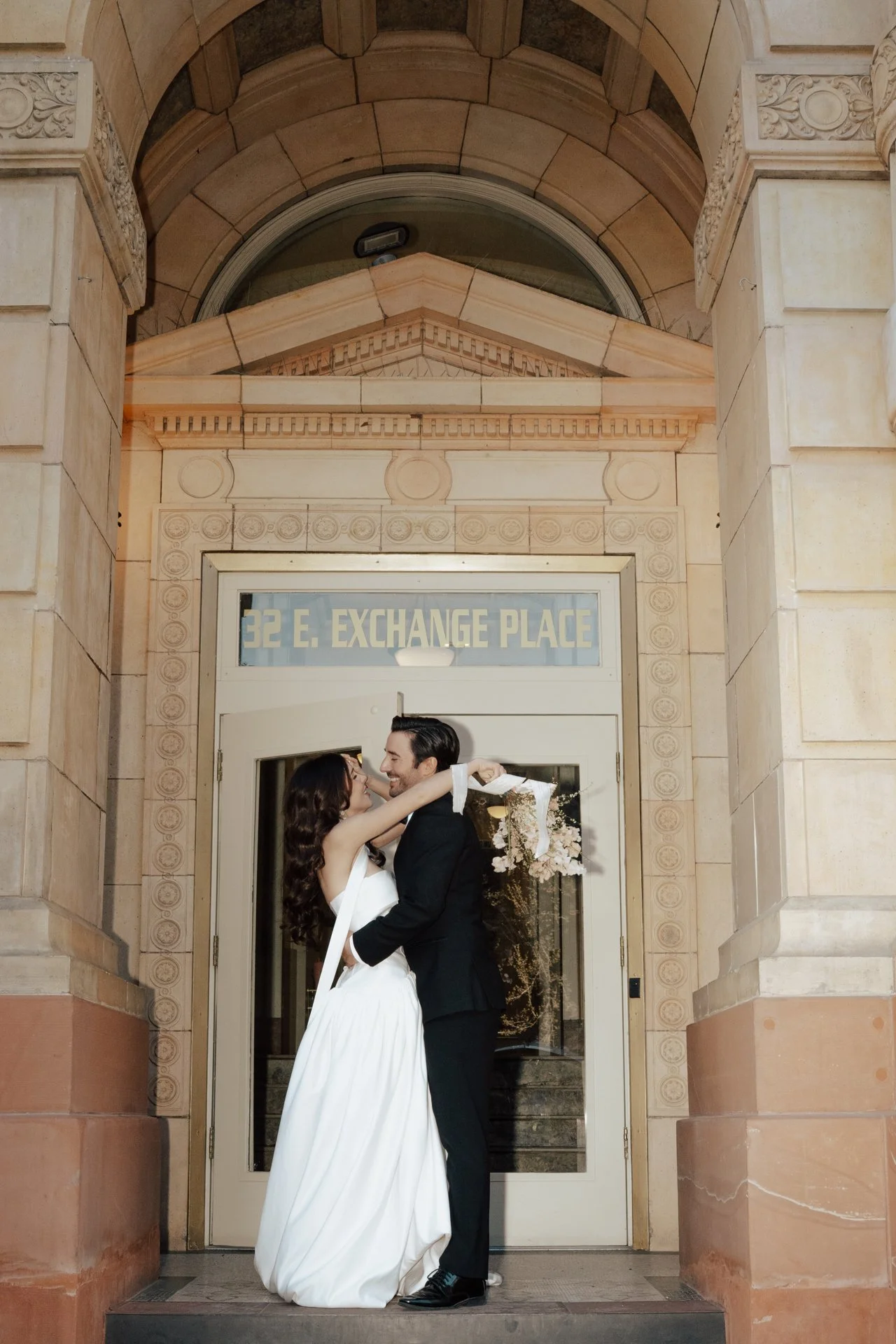 Bride and Groom in classic elegant wedding attire surrounded by beautiful stonework architecture during a downtown formals photoshoot - Poise and Ivy Imagery