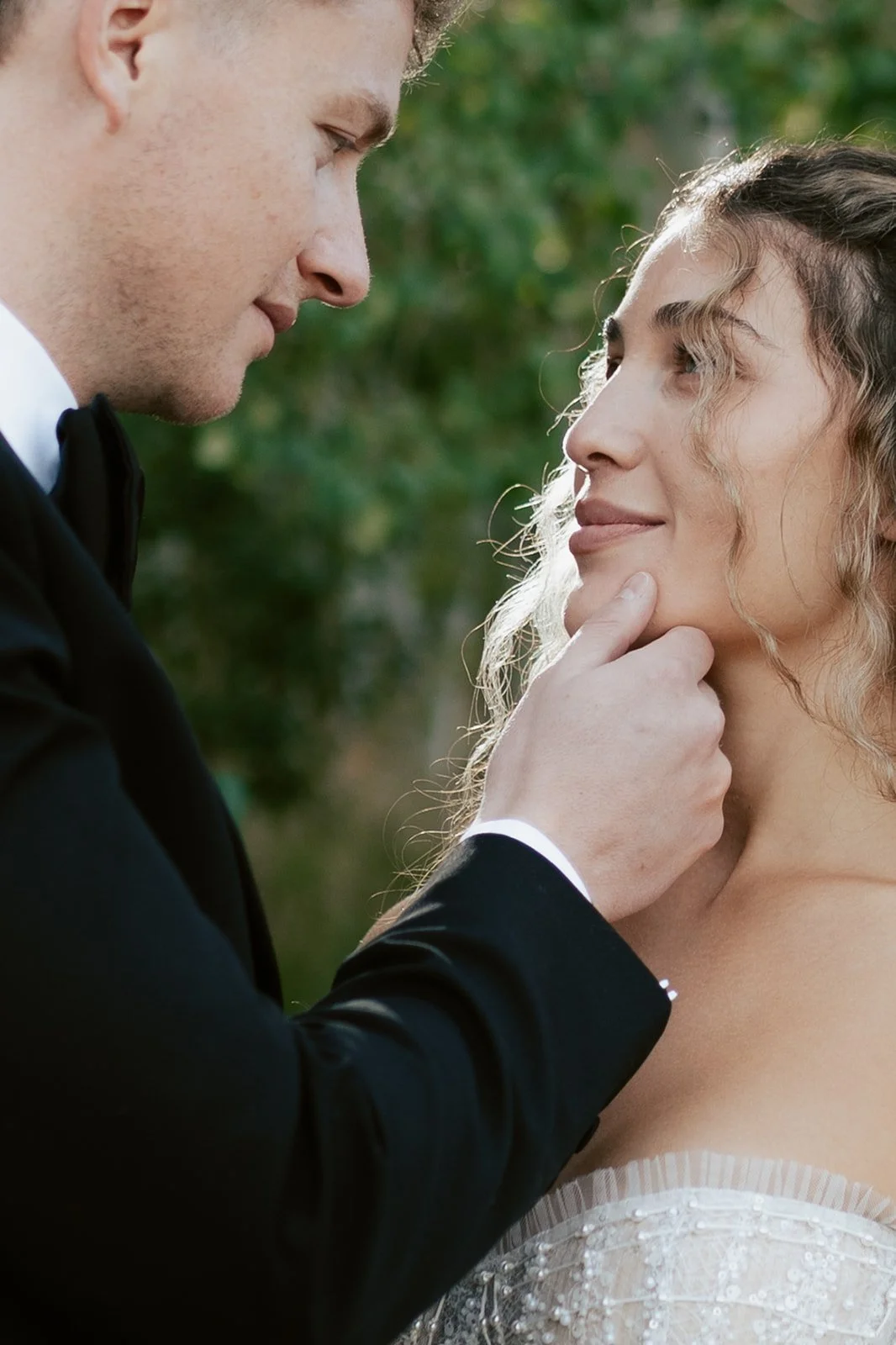 A groom gently holds his bride's face as they embrace each other