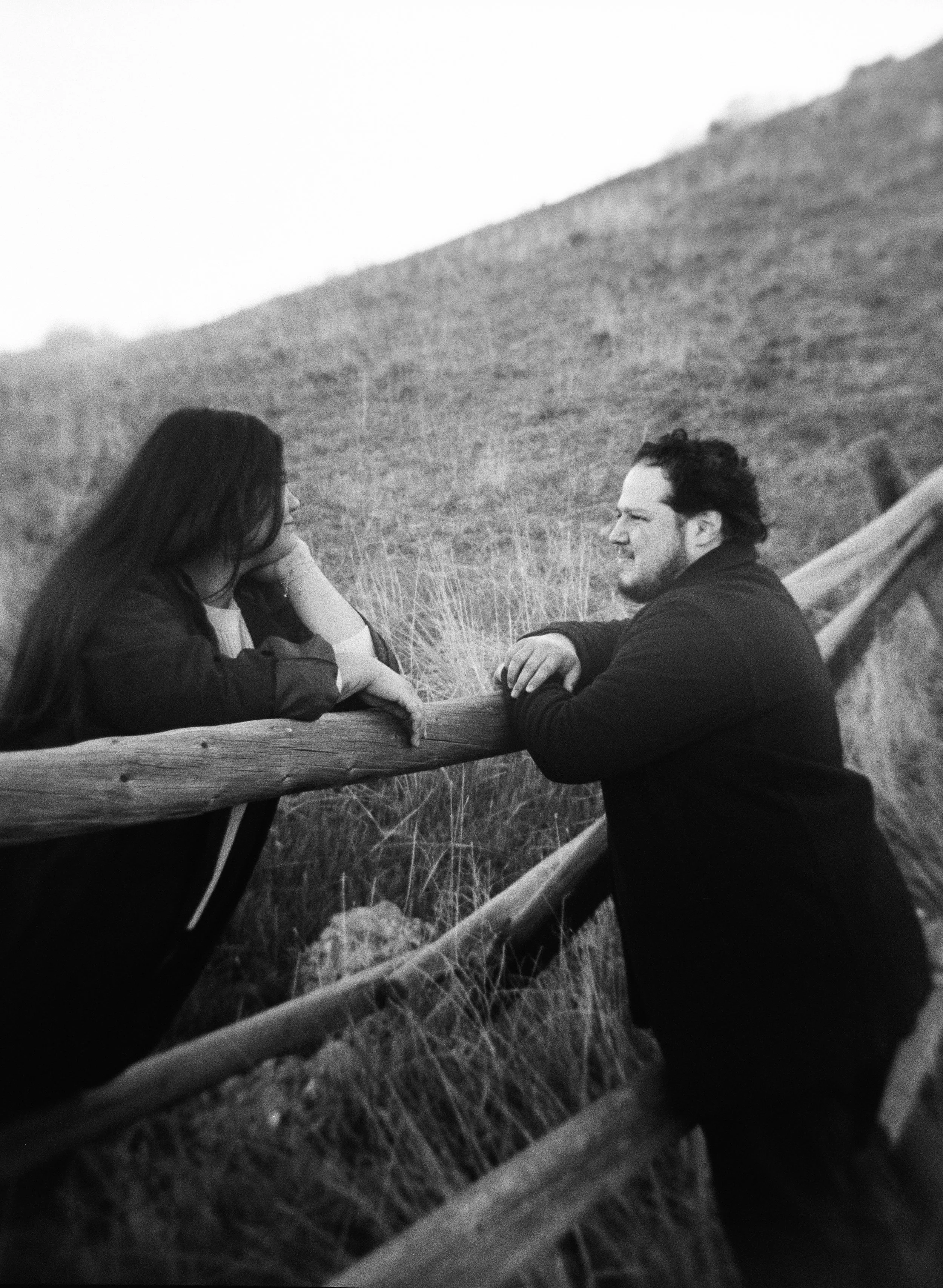 A couple stands together in a softly lit grassy field on black and white medium format film - photography by Poise and Ivy Imagery