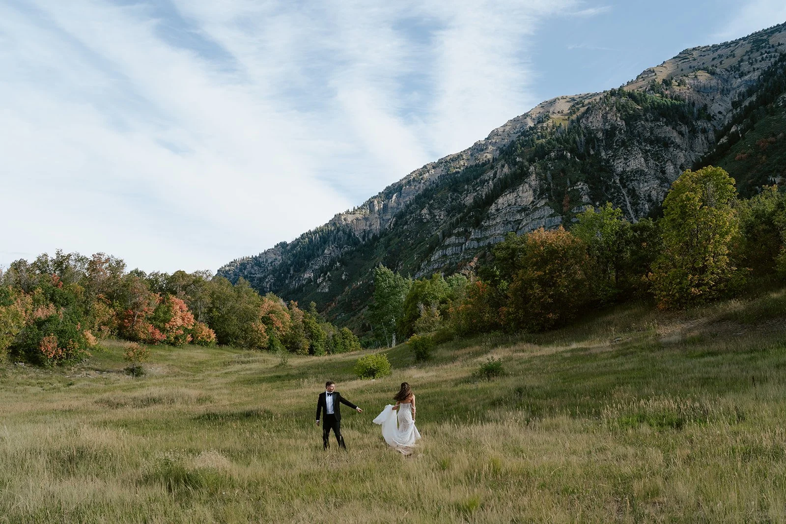 a bride and a groom run together through a sunlit meadow. the bride wears a beaded wedding gown and the groom wears a tuxedo. Photography by Poise and Ivy Imagery