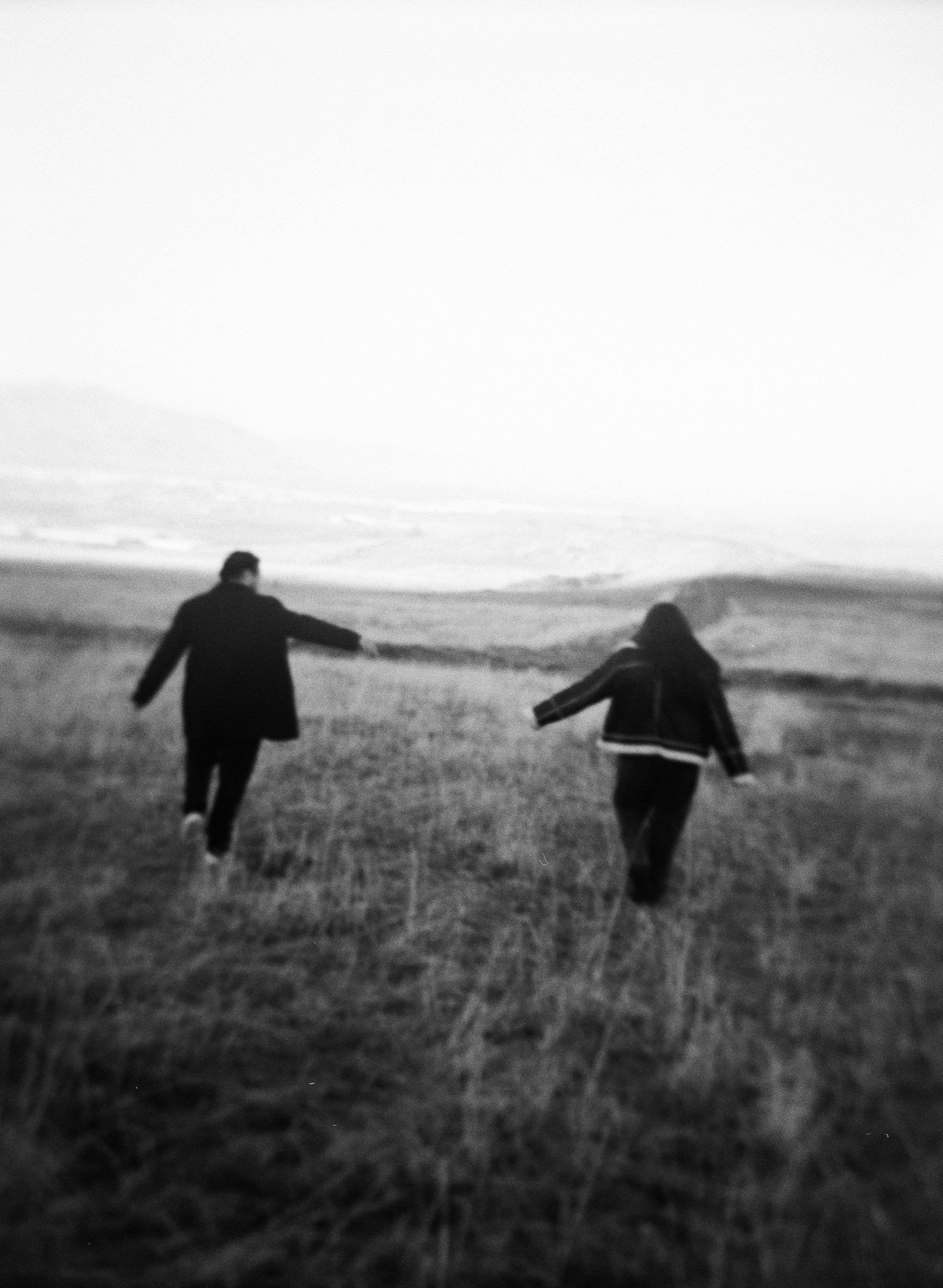 A couple stands together in a softly lit grassy field on black and white medium format film - photography by Poise and Ivy Imagery