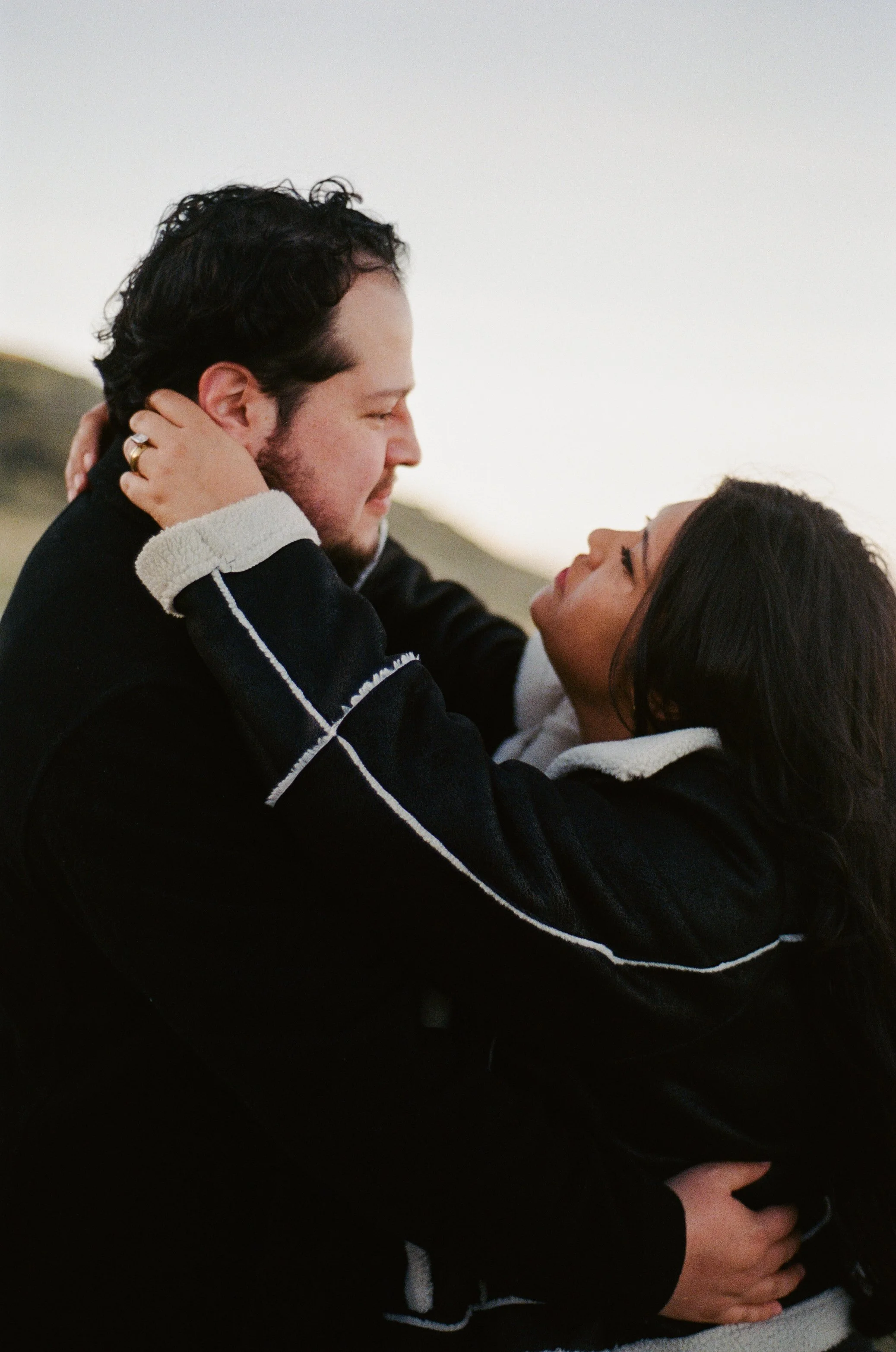 A couple stands together in a softly lit grassy field, photographed on color negative film by Poise and Ivy Imagery