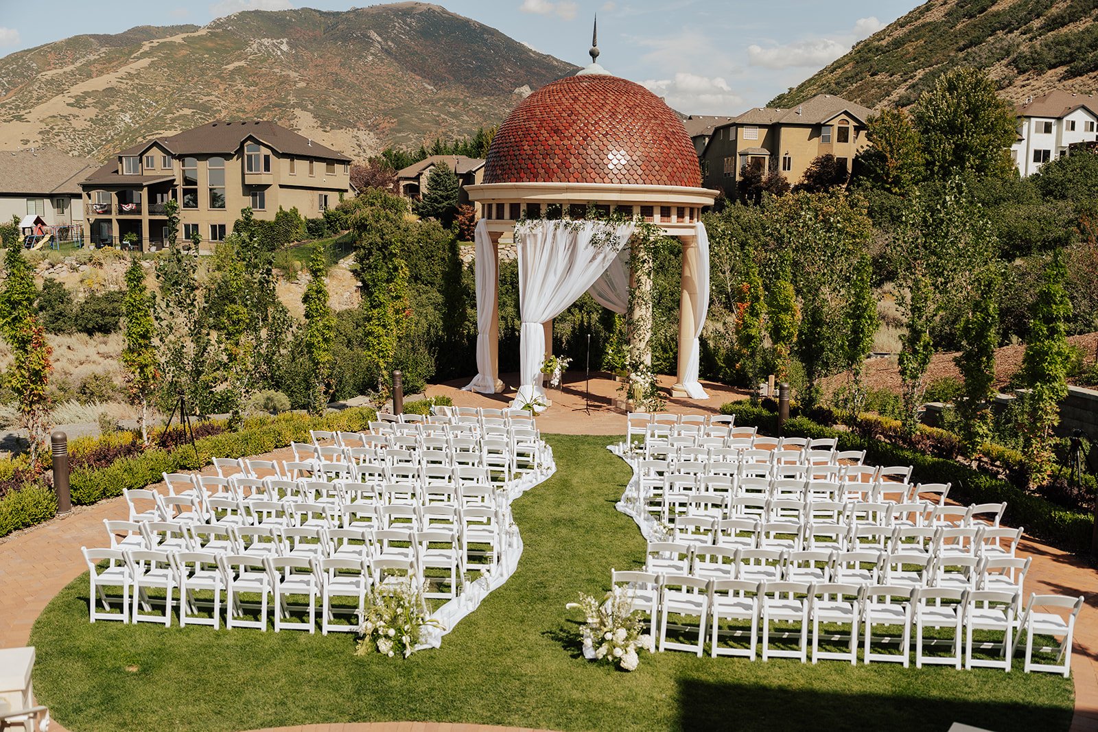 Wedding ceremony set up details featuring a gazebo with marble pillars decorated with green and white flowers and vines as well as white drapery - photography by Poise and Ivy Imagery