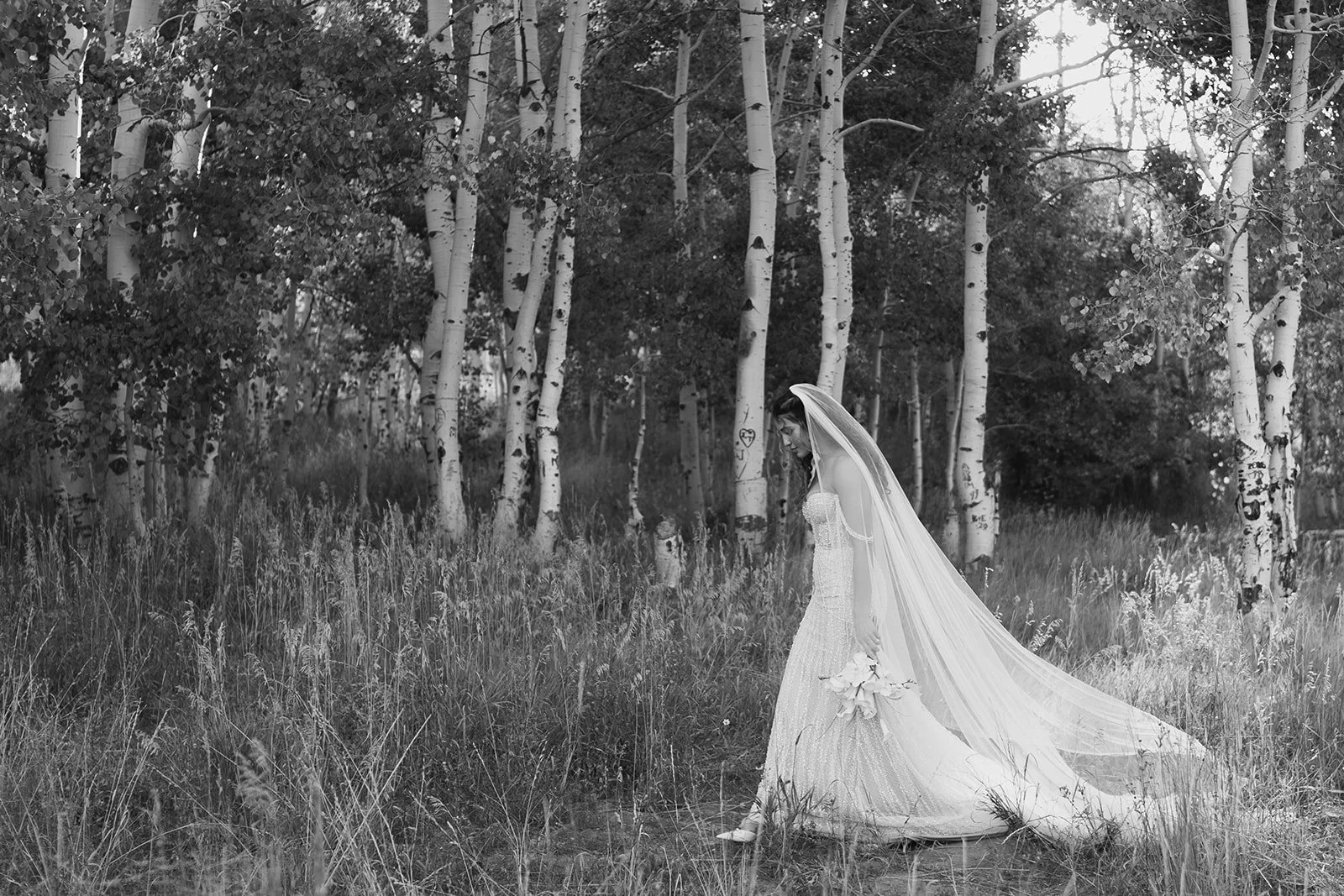 bride in a beaded pearl embroidered wedding gown walks in a meadow. photo in black and white, taken by Poise and Ivy Imagery