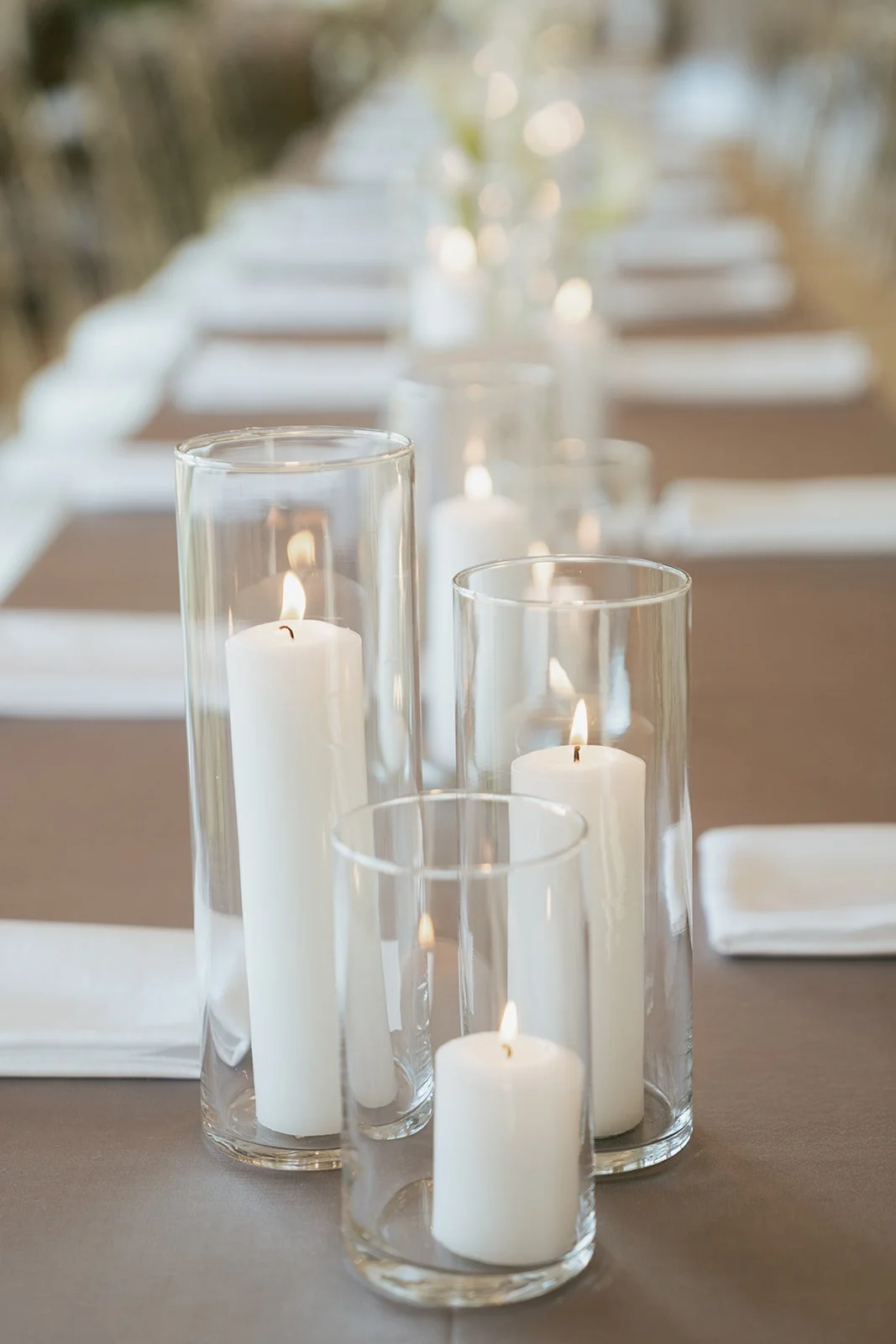 wedding reception details featuring white pillar candles in glass vases against a soft grey tablecloth - Photography by Poise and Ivy Imagery, Wedding Design by Britt Warnick Designs