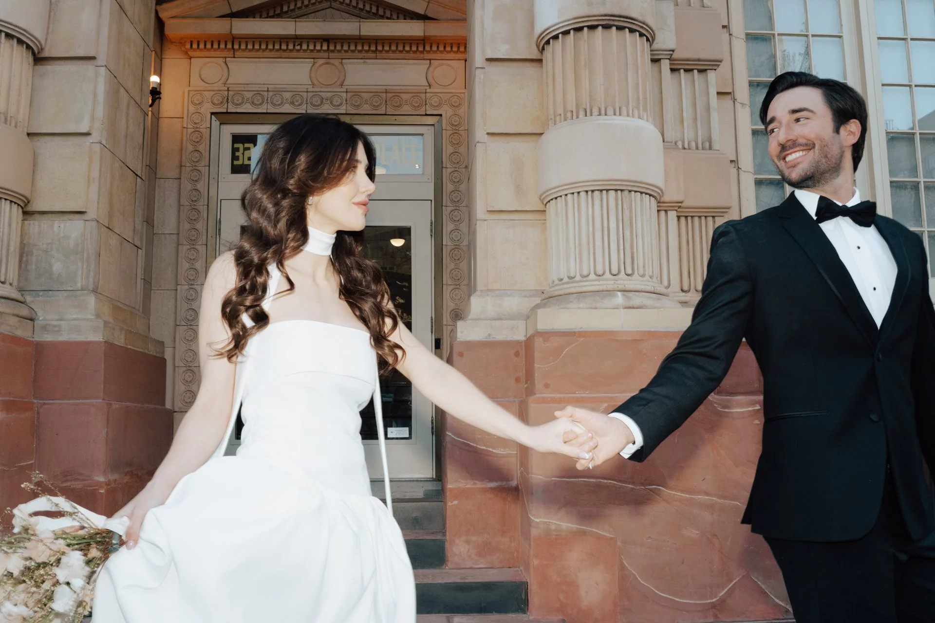 Bride and Groom in classic elegant wedding attire surrounded by beautiful stonework architecture during a downtown formals photoshoot - Poise and Ivy Imagery