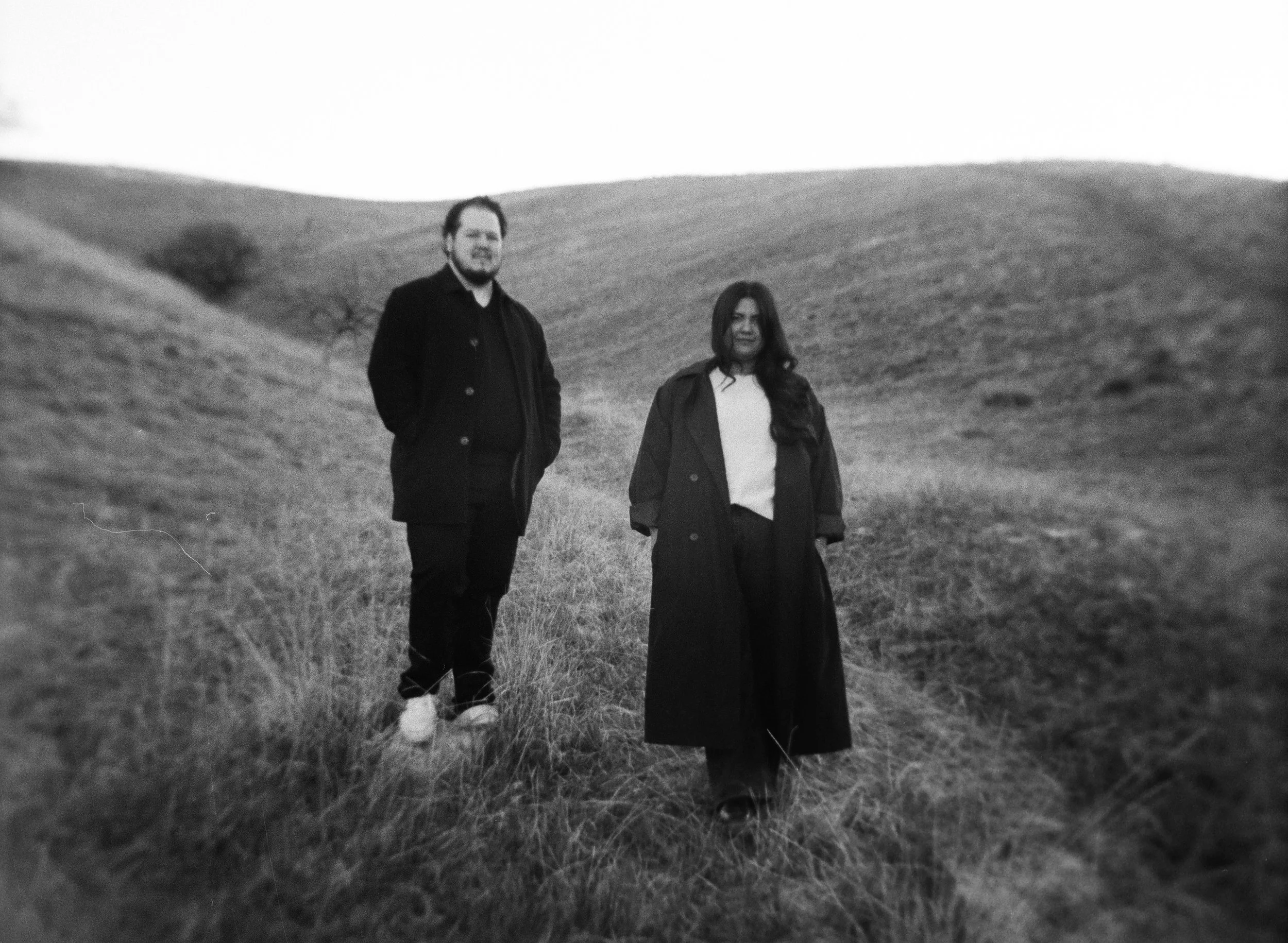 A couple stands together in a softly lit grassy field on black and white medium format film - photography by Poise and Ivy Imagery