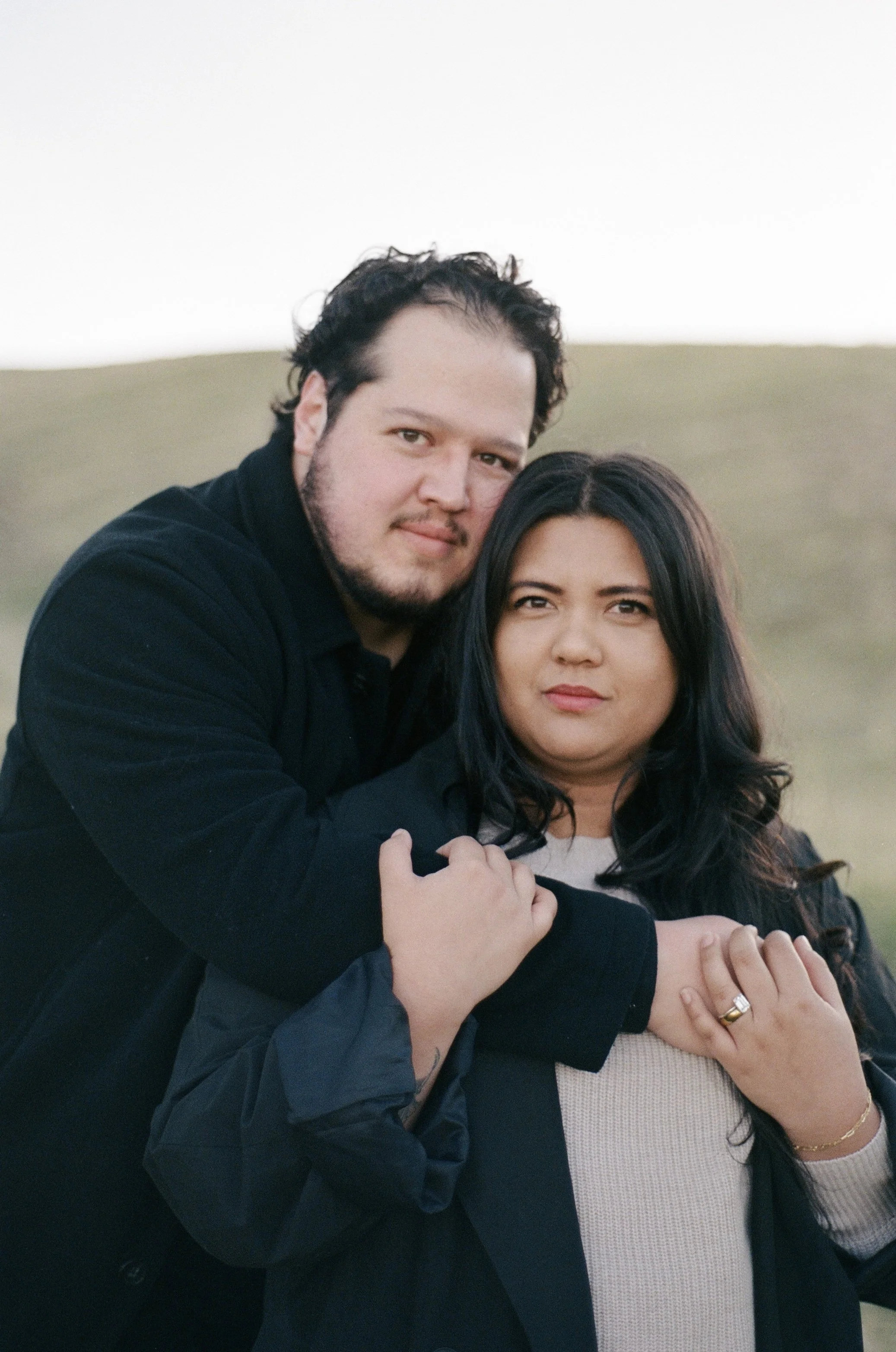 A couple stands together in a softly lit grassy field, photographed on color negative film by Poise and Ivy Imagery