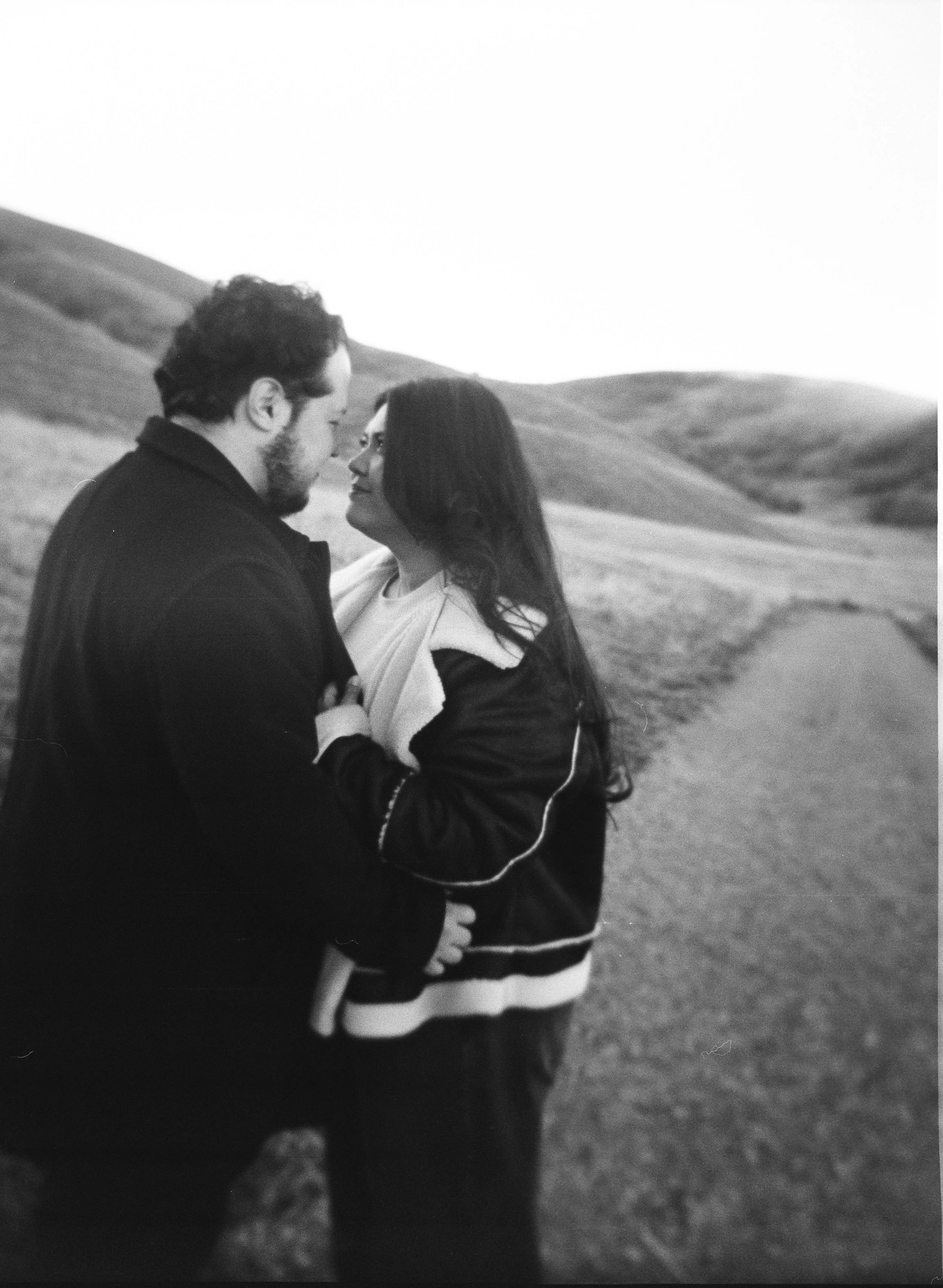 A couple stands together in a softly lit grassy field on black and white medium format film - photography by Poise and Ivy Imagery