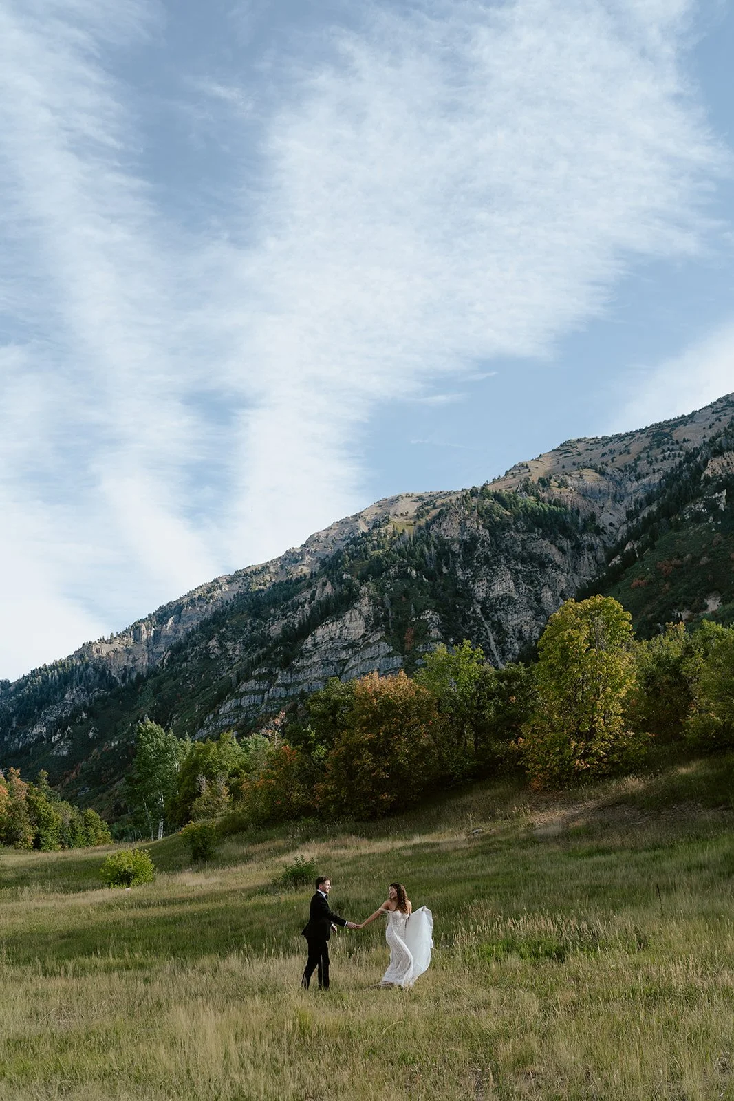 a bride and a groom run together through a sunlit meadow. the bride wears a beaded wedding gown and the groom wears a tuxedo. Photography by Poise and Ivy Imagery