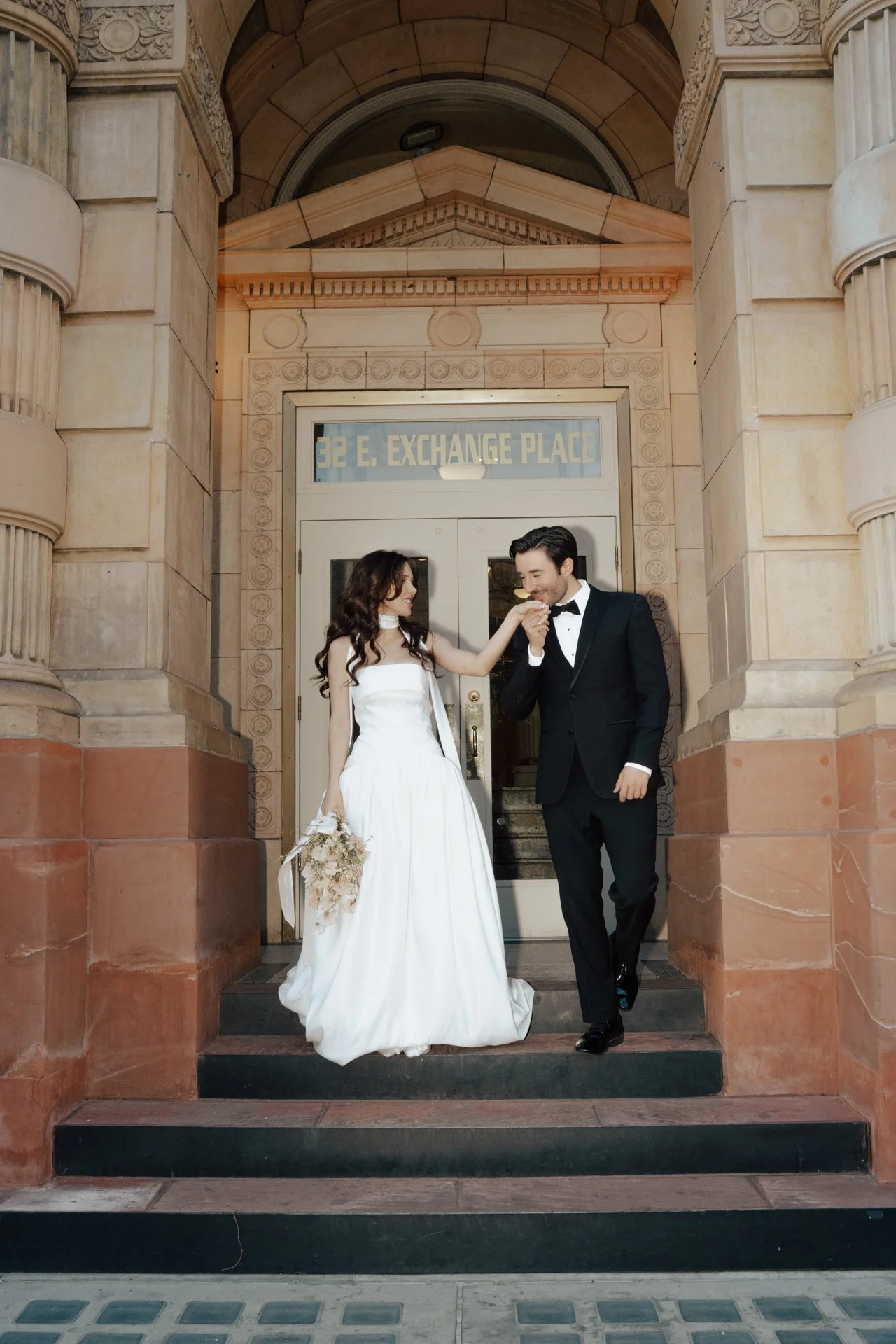 Bride and Groom in classic elegant wedding attire surrounded by beautiful stonework architecture during a downtown formals photoshoot - Poise and Ivy Imagery