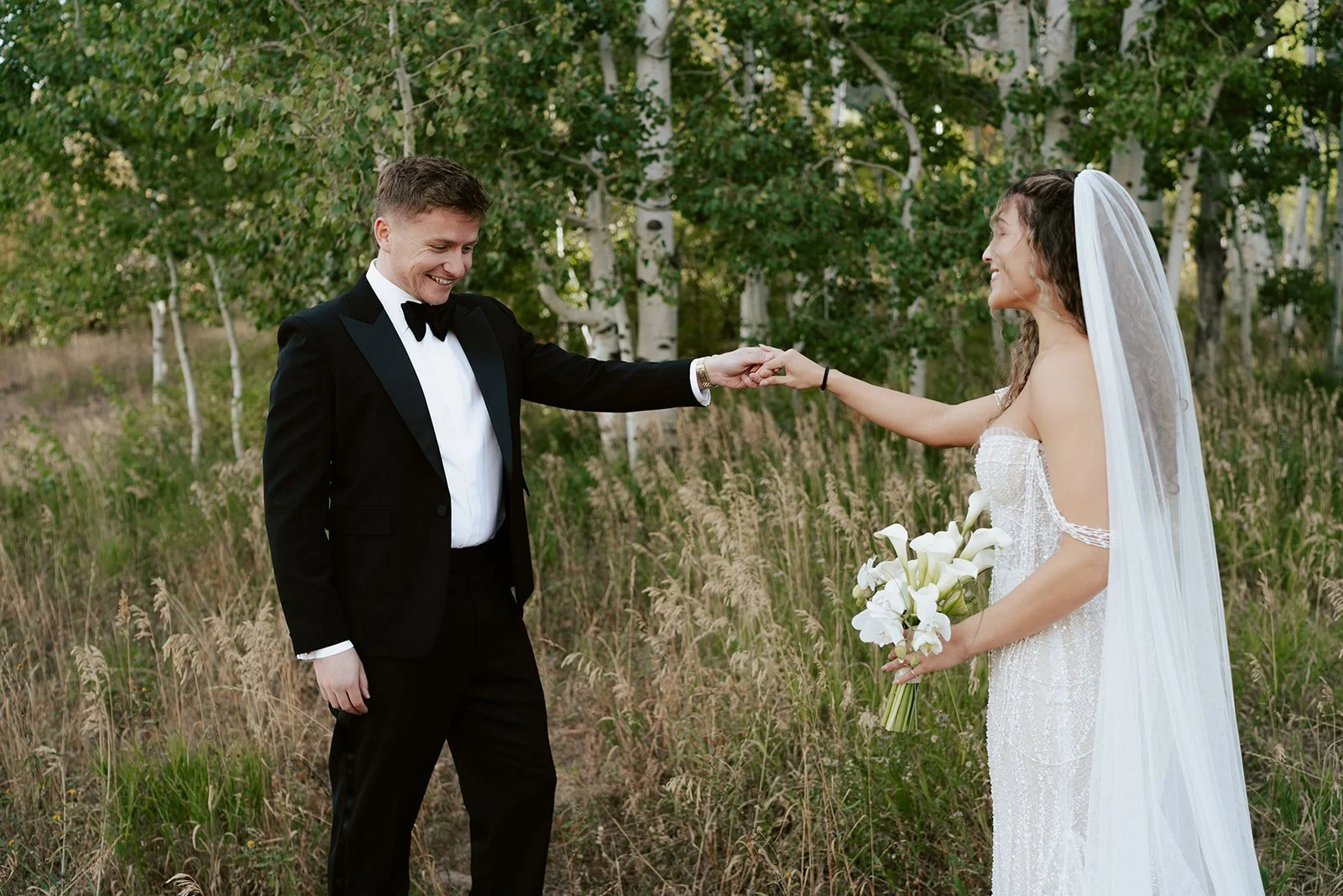 a bride and a groom stand together in a lush aspen grove. the bride wears a beaded wedding gown with a bridal veil and the groom wears a tuxedo. Photography by Poise and Ivy Imagery