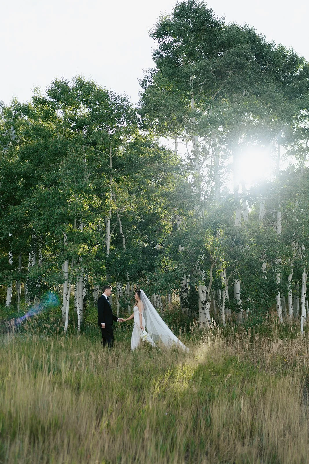 a bride and a groom stand together in a lush aspen grove. the bride wears a beaded wedding gown and the groom wears a tuxedo. Photography by Poise and Ivy Imagery
