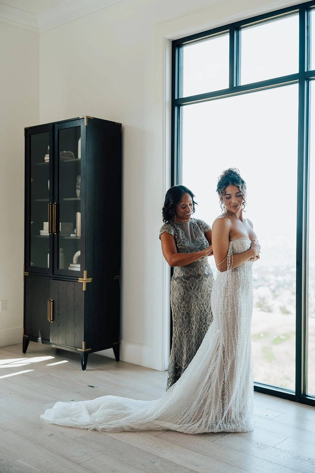 a bride getting ready for her marriage ceremony while her mother helps her into her beaded wedding dress- Photography by Poise and Ivy Imagery