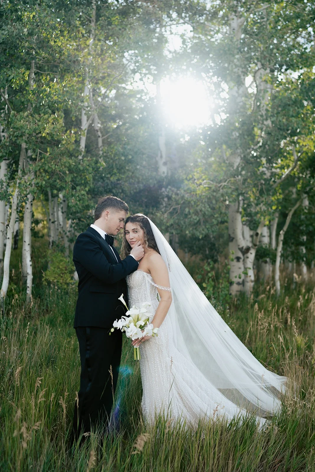 a bride and a groom stand together in a lush aspen grove. the bride wears a beaded wedding gown and the groom wears a tuxedo. Photography by Poise and Ivy Imagery