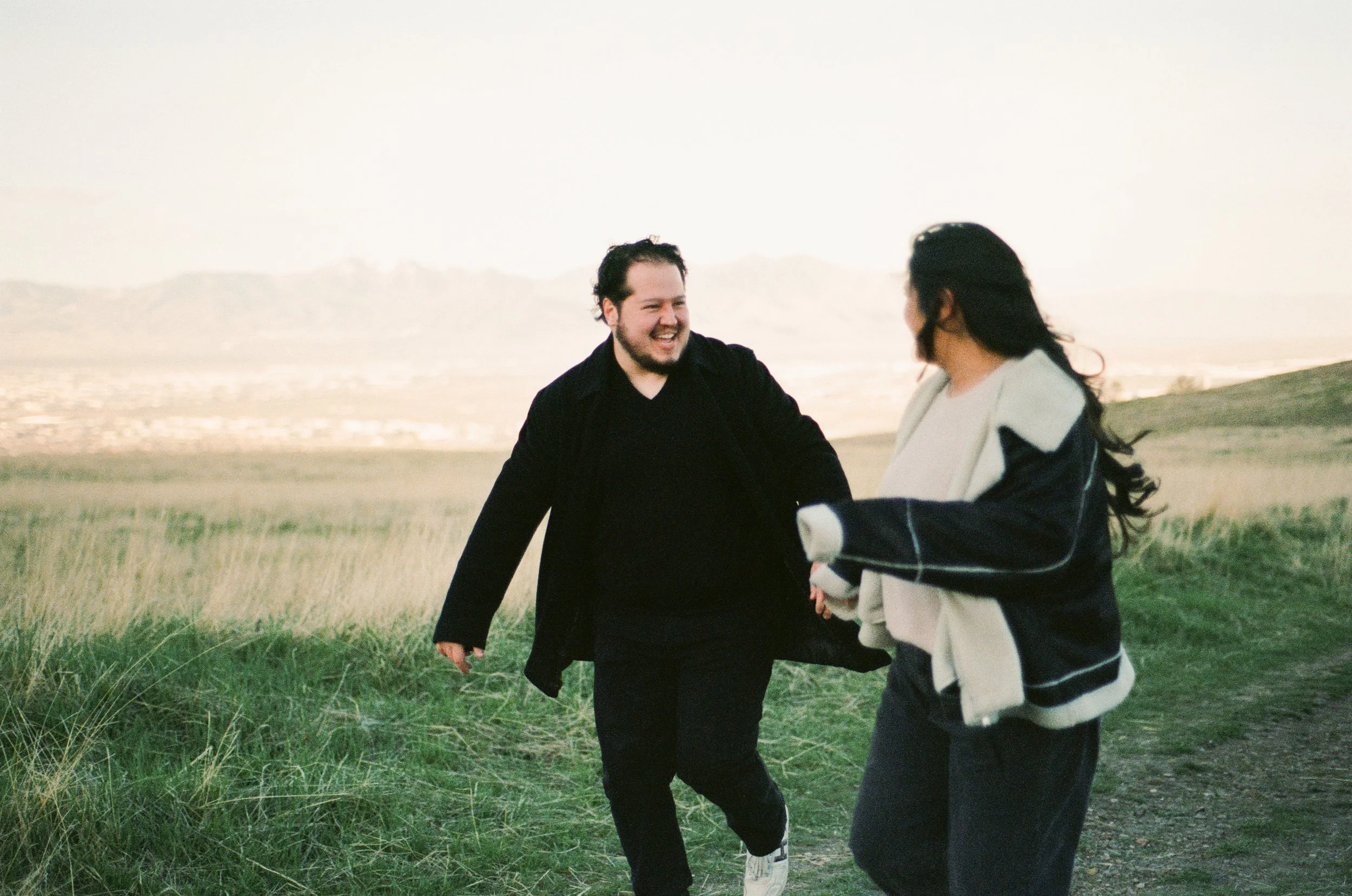 A couple stands together in a softly lit grassy field, photographed on color negative film by Poise and Ivy Imagery
