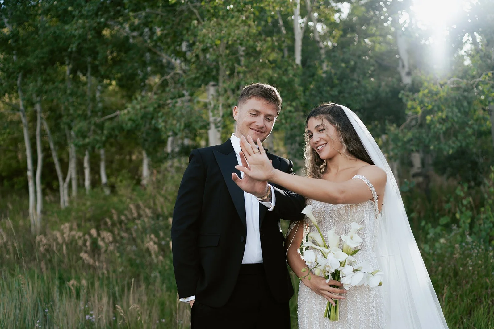 a bride and a groom stand together in a lush aspen grove. the bride wears a beaded wedding gown and the groom wears a tuxedo. Photography by Poise and Ivy Imagery
